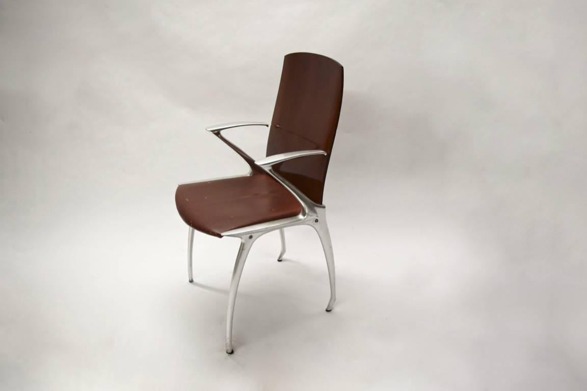 Set of six dining chairs all with arms upholstered seats and a slightly curved backrest in wood. The frame is made of sleekly curved legs and arms in polished cast aluminum and a seat in distressed leather.