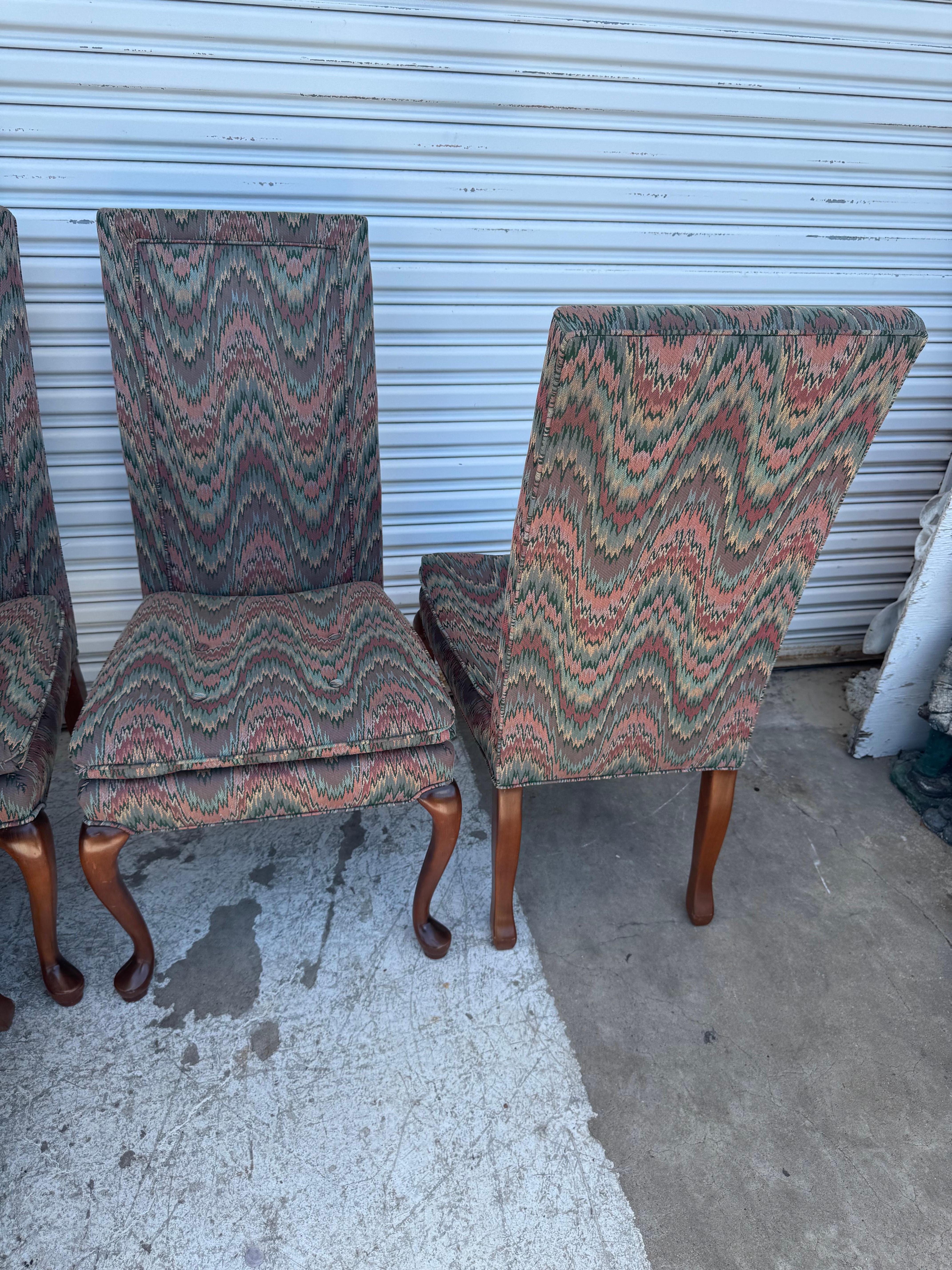 set of six vintage-style high-back dining chairs, featuring a distinctive zigzag or flame-stitch upholstery pattern in earthy tones of green, red, and beige. The fabric gives them a classic, retro appeal, reminiscent of mid-century or late