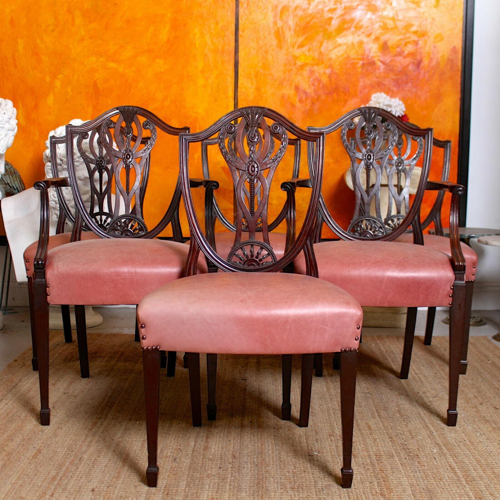 An attractive set of six carved mahogany dining chairs in the Hepplewhite manner.

The shield shaped backs framing pierced splats carved with wheat sheaf swags and floral medallions, the leather studded upholstered seats raised on square tapering