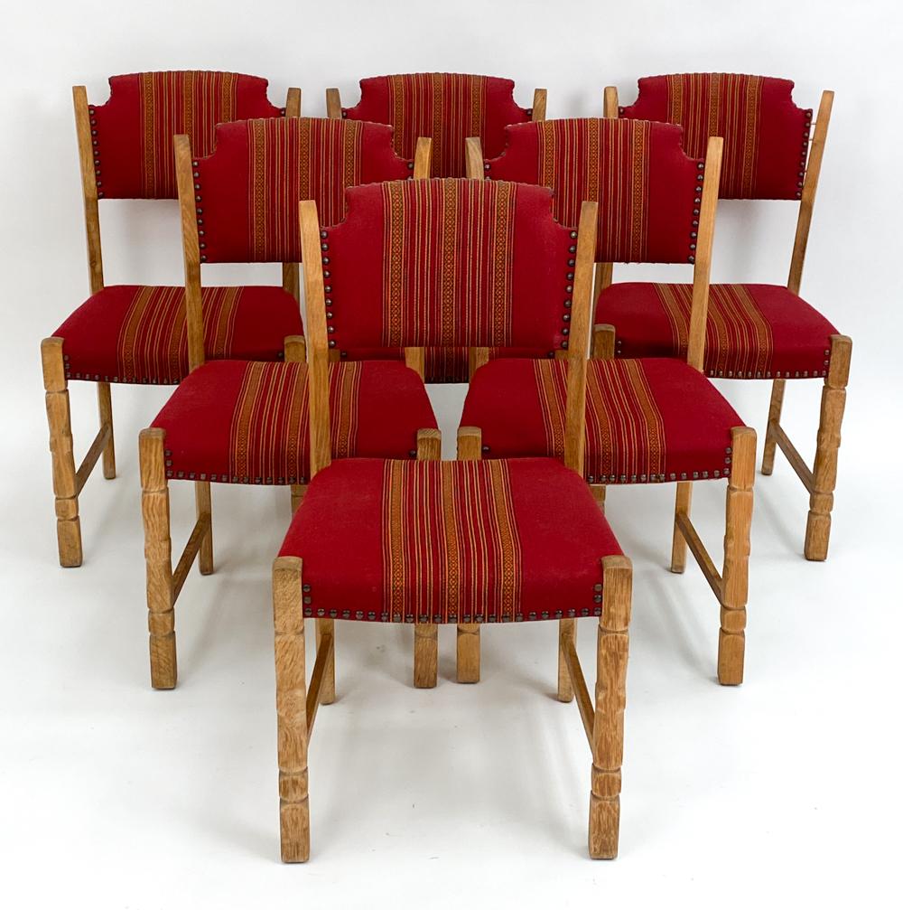 A set of six Danish midcentury dining side chairs by designer Henning Kjaernulf, well-renowned for his iconic farmhouse-inspired carved oak furniture designs, c. 1960s. These charming Provincial chairs feature low sculpted backs, an upholstered