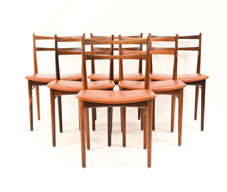 A handsome set of Danish mid-century dining chairs designed by Henry Rosengren Hansen for Brande Mobelindustri. Featuring elegant rosewood curved ladder-back design frames with cognac leather seats. Marked with manufacturer's stamp underneath.