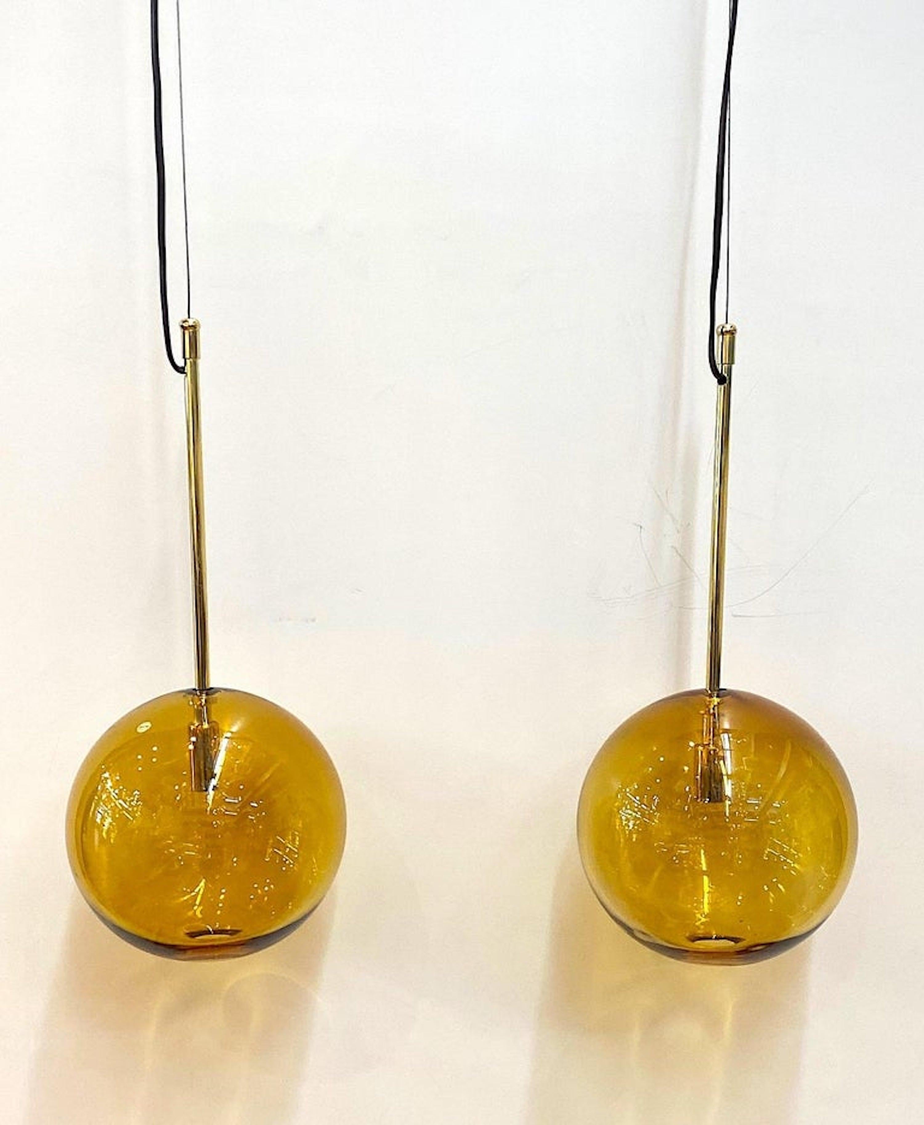 Italian hand blown Murano golden amber glass globe shade pendant lights. Six available. Each globe shade is 7 inches in diameter and rests on a brass rod for a 12 inch height. From the top of the rod is a steel cable. Just below on the side exits