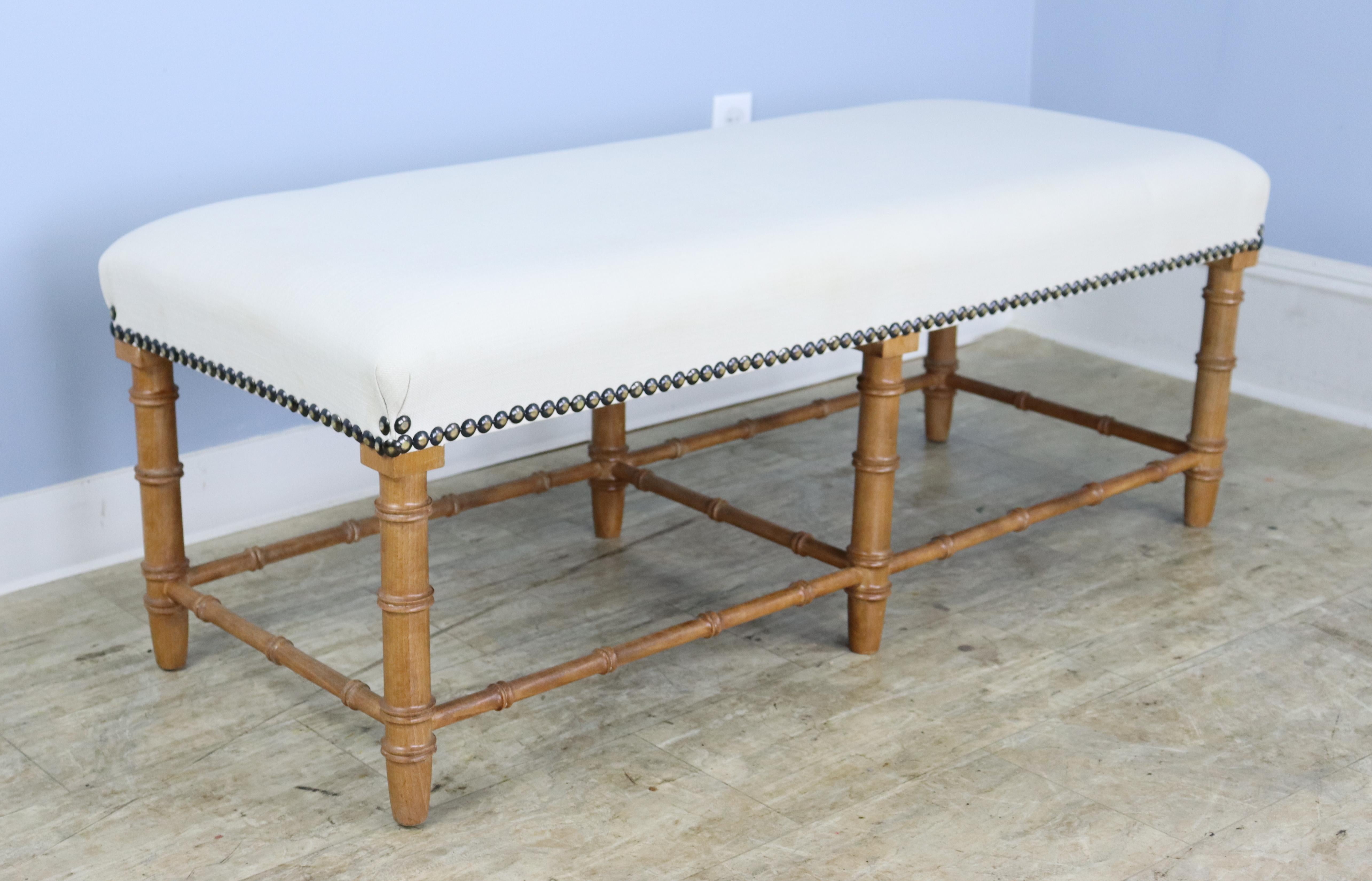 A long comfortable bench or stool in elegant faux bamboo, possibly craved of English Golden Oak. A classic look, newly uphostered in cream linen.