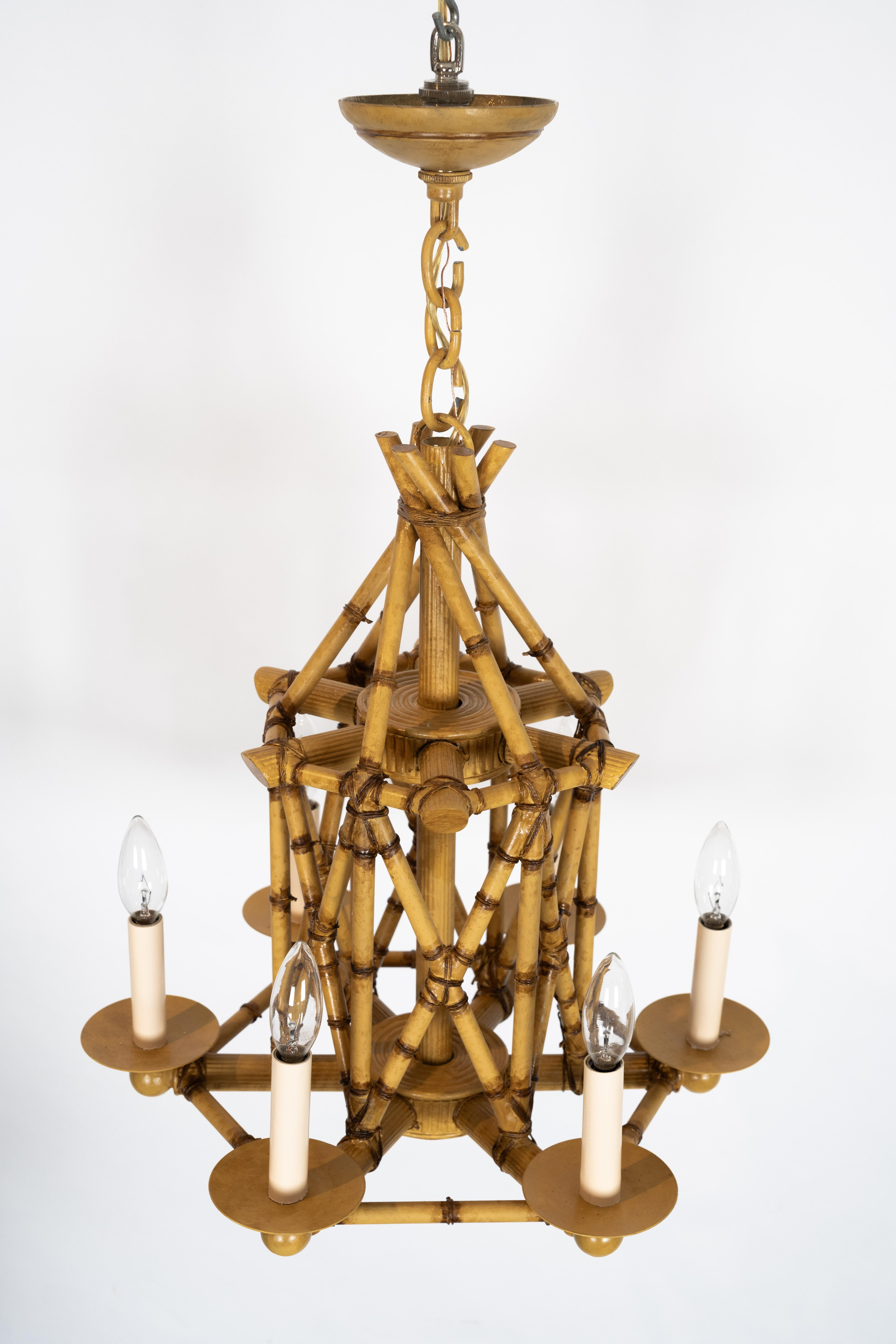 A six-light faux bamboo chandelier. Featuring an intricately constructed cage, formed by cross-banded sections of hand-painted faux bamboo made from brass. With bobeches issuing six candle sleeves.