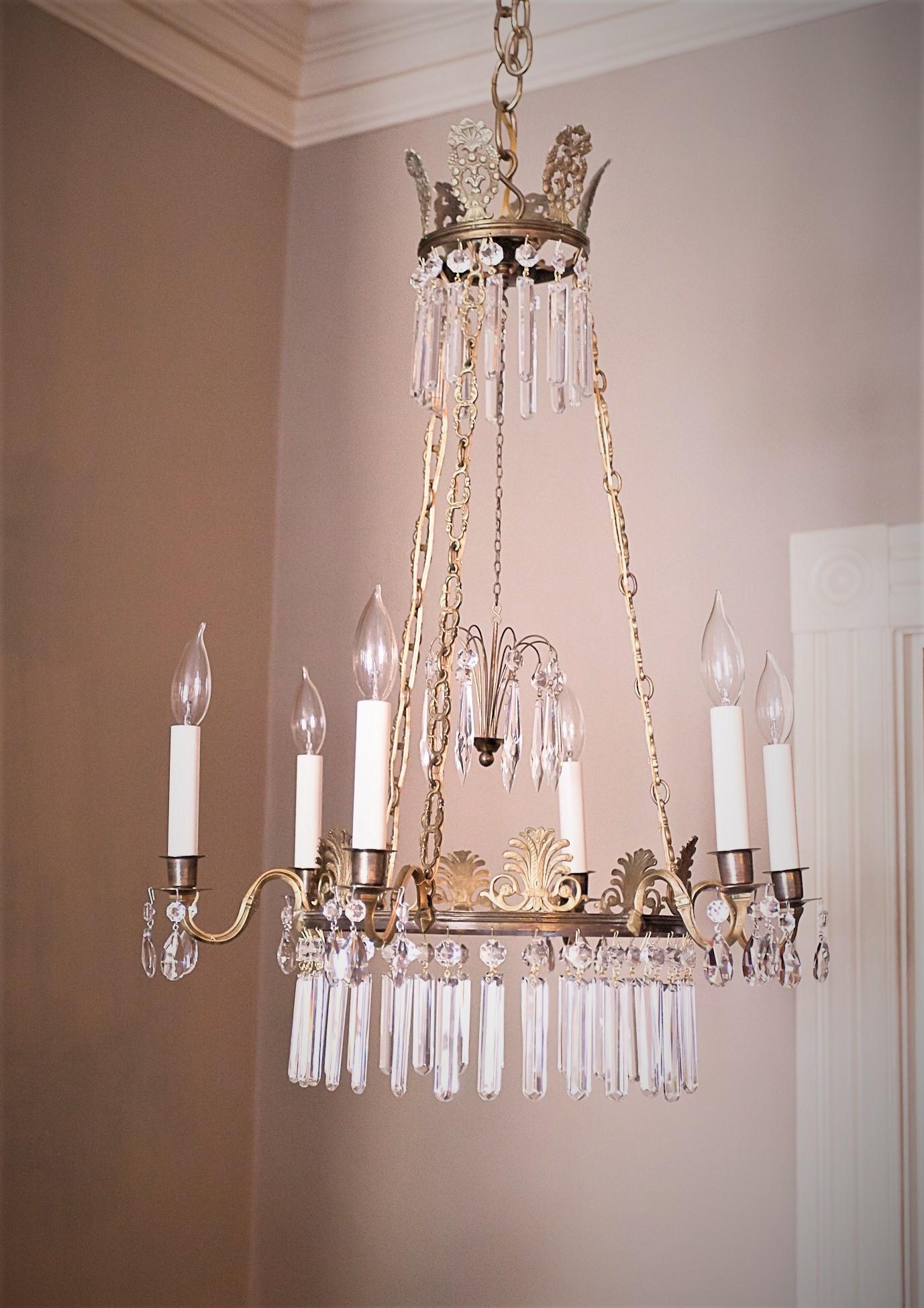 This Swedish neoclassical style fixture is hand cast aged brass with lead crystal prisms with gilt anthemion’s. Originally candle-burning, now skilfully French (externally) wired. Chandelier can be shortened if desired. Hanging hardware, ceiling cap