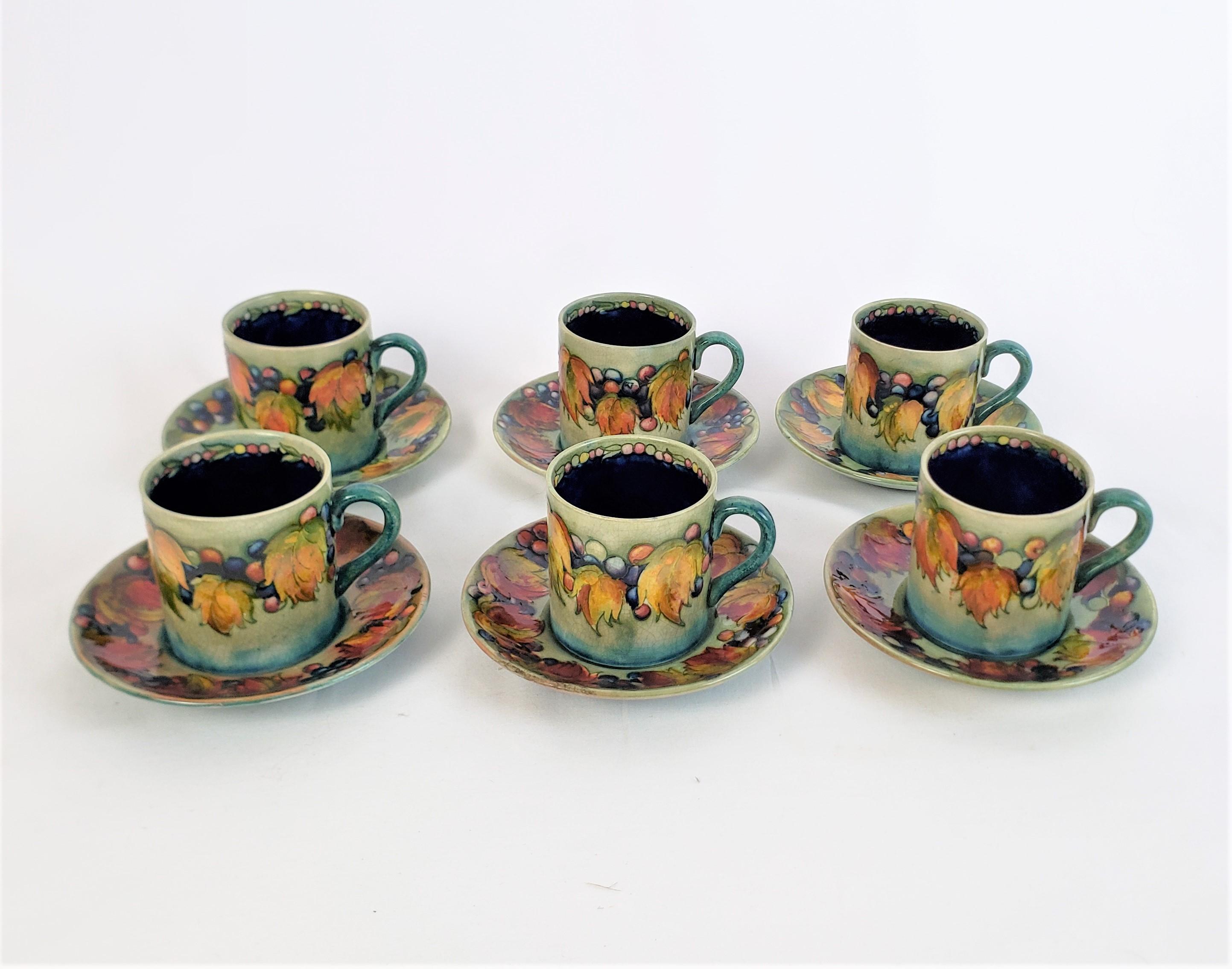 This set of six demitasse cups and saucers were made by the renowned Moorcroft factory of England in approximately 1940 in their signature Leaf and Berry pattern. The cups are done with a green ground with cobalt blue interior and four of the