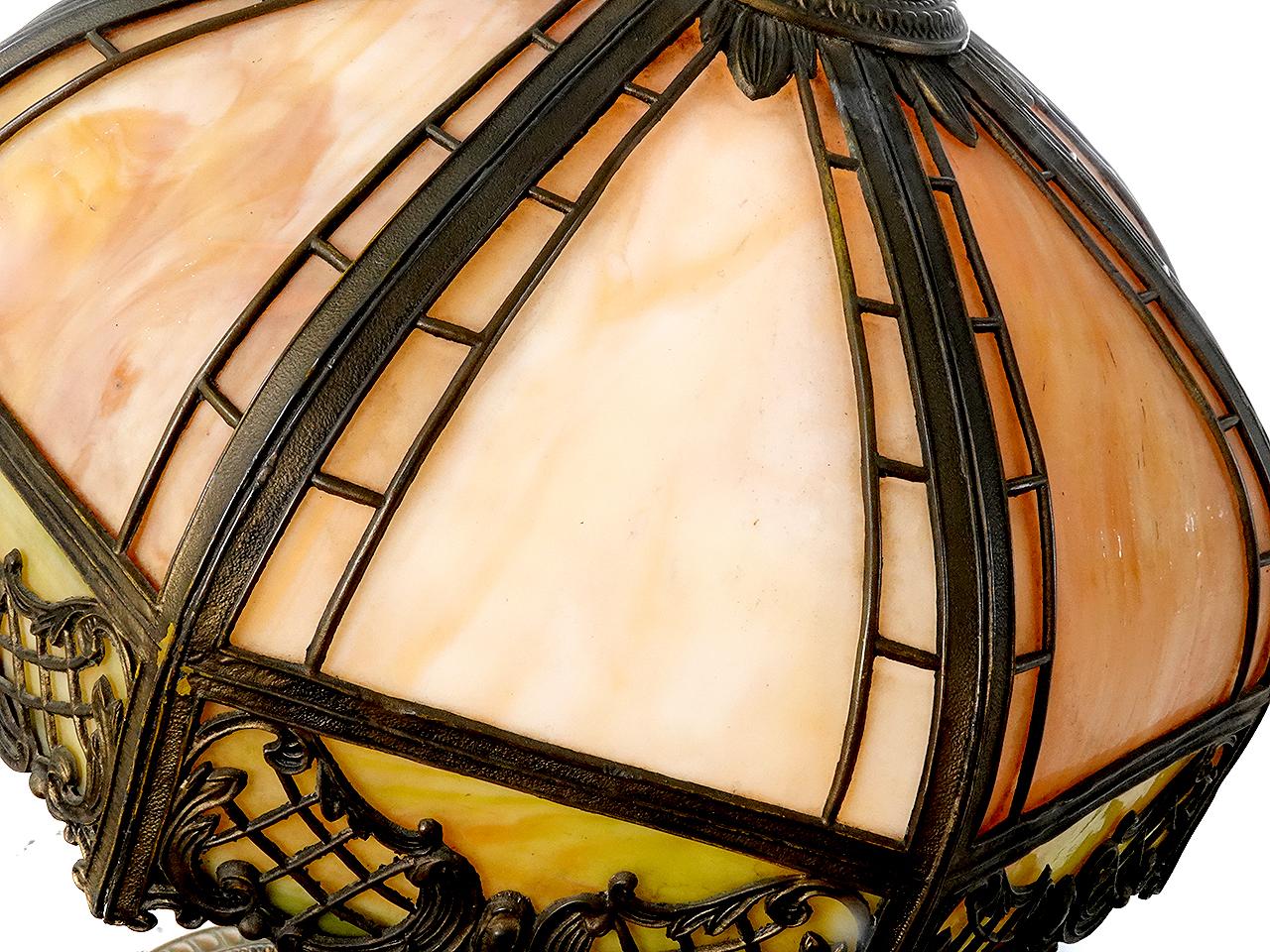 This is a nicely designed Arts and Crafts table lamp. It has a curved shade with 6 unique latticework filigree overlays. Each slump glass (curved) panel features a cream -  amber variegated glass with some hints of moss green. It is lit by one E26