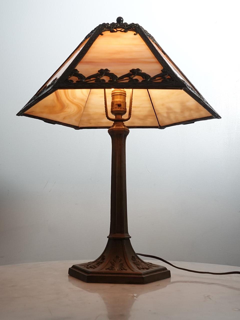 This is a nicely designed Arts and Crafts table lamp. Its simple and clean with a tented shape and 6 cast floral filigree panels. Each panel features a cream -  amber variegated glass and is lit by a single E26 bulb