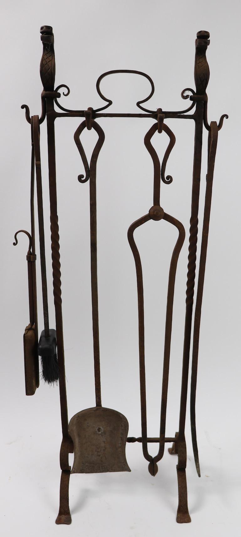 Handwrought iron Gothic Revival, Arts & Crafts, Mission period fireplace tool set with fantastic animal finials, and rattail handles.
This set includes a poker, tongs, shovel, brush, unusual ash receptacle, and the stand. Currently in all-over rust