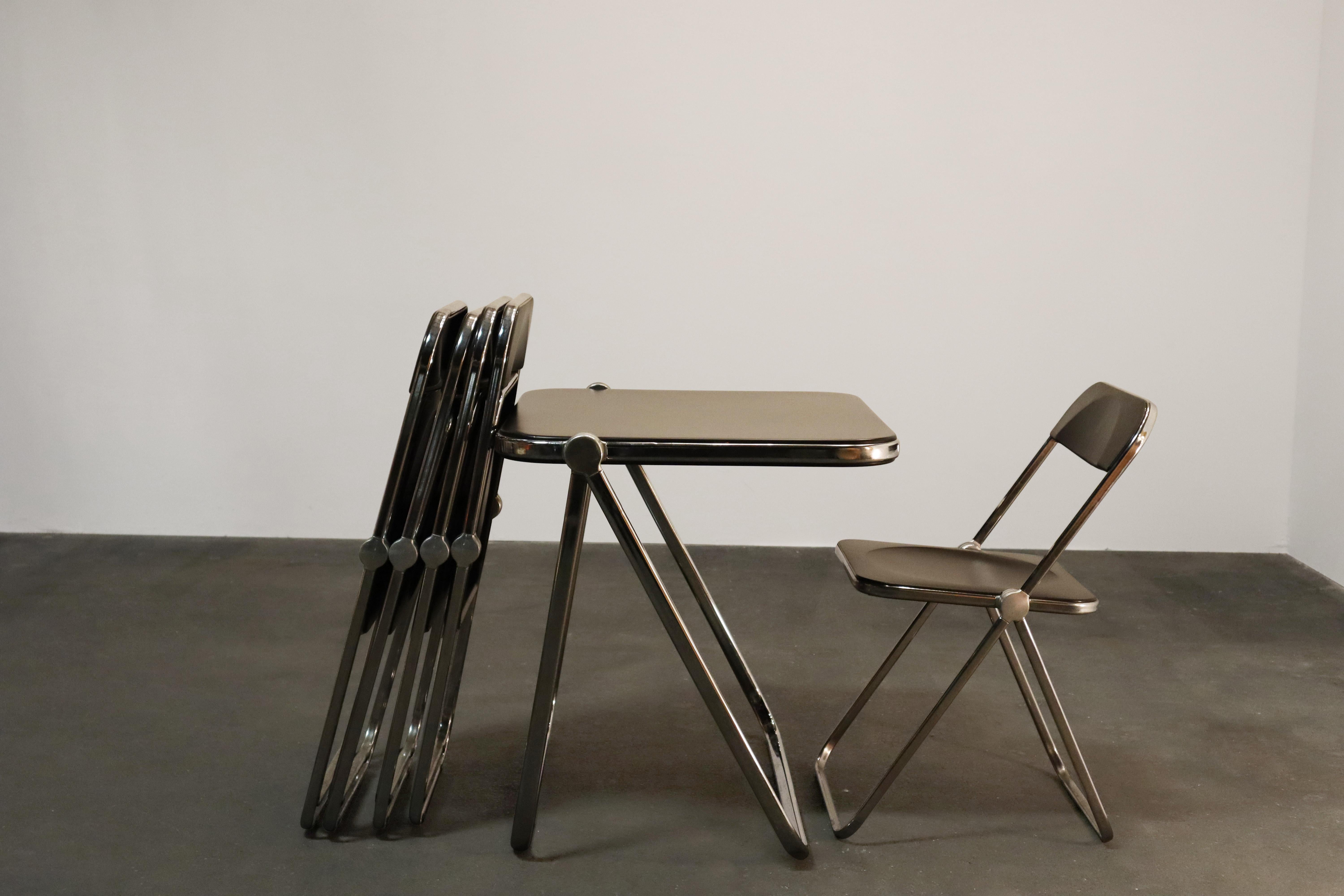 Six-piece set of Space Age chrome and brown lucite folding chairs (5) and table (1) designed by Giancarlo Piretti for Castelli, Italy. 

With steel frame, seat and back in brown lucite, it represents the realization of “democratic design” and is