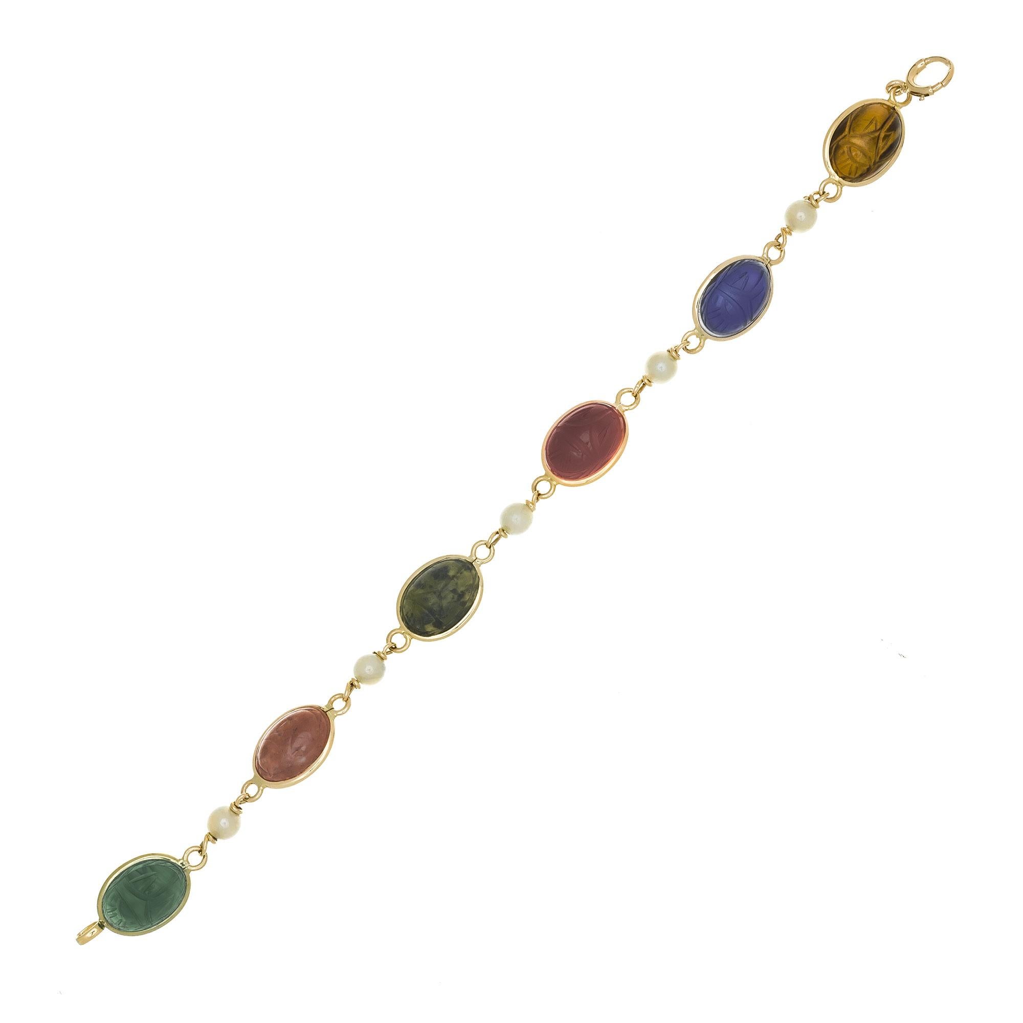 Vintage 1950's 14k yellow gold oval scarab link bracelet with 5 white/ gray hue 5mm pearls. 7.5 inches long.  

5 white gray hue pearls, 5mm
6 Tigers eye, lapis, carnelian, bloodstone, coral, nephrite oval scarabs 
14k yellow gold 
Stamped: 14k
10.8