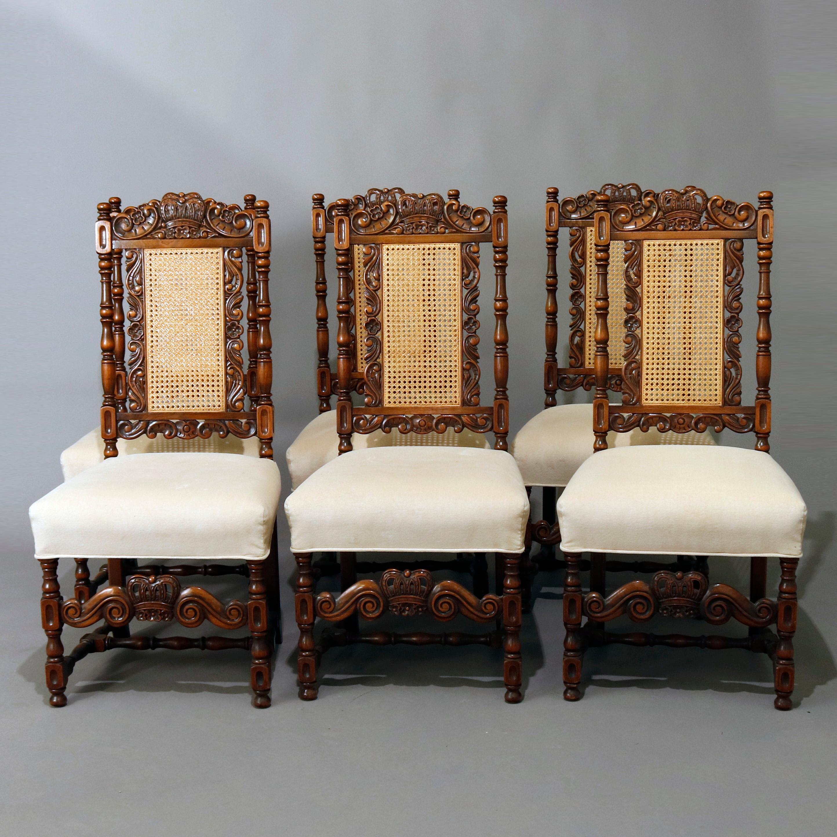 A vintage set of six Gothic style dining chairs by Kittinger feature heavily carved walnut frames with crown crests flanked by gadroon and foliate elements surmounting pressed cane backs with turned columns and upholstered seats raised on turned