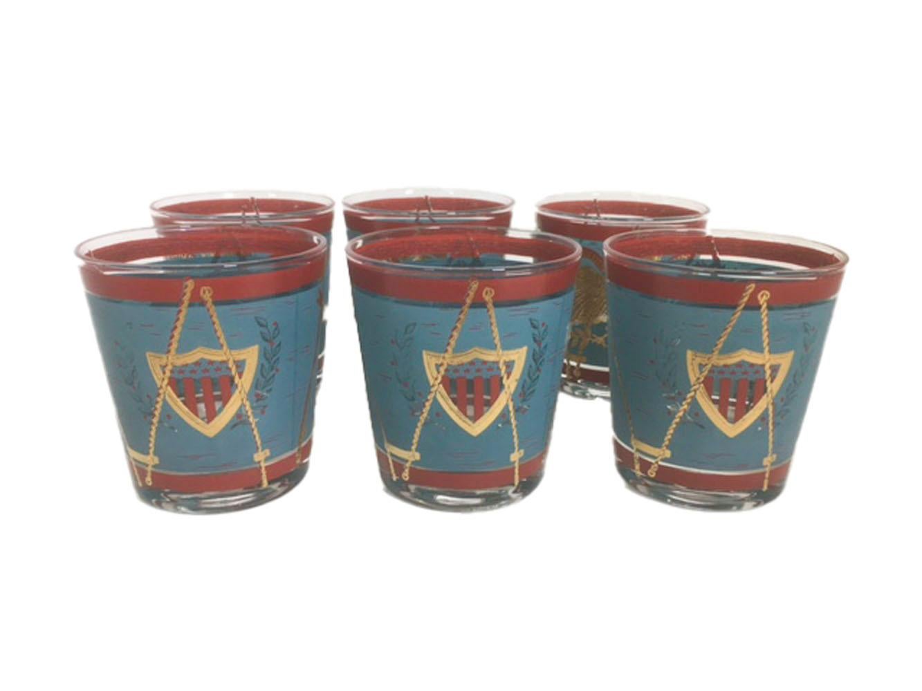 Mid-Century Modern old fashioned glasses decorated as parade drums in teal and red enamel with 22 karat gold.
The front with a large patriotic eagle below a banner with the motto E Pluribus Unum. The eagle with a stars and stripes shield on its