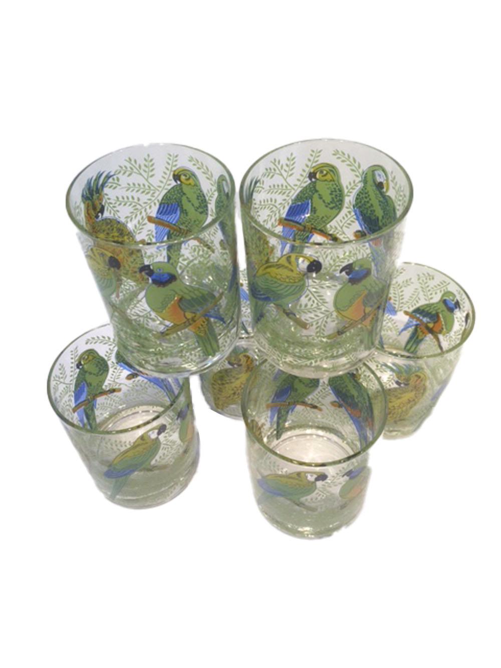 Set of six rocks glasses with parrots or macaws with brightly colored feathers in a background of bright green tropical foliage. Private labeled for Neiman-Marcus.
