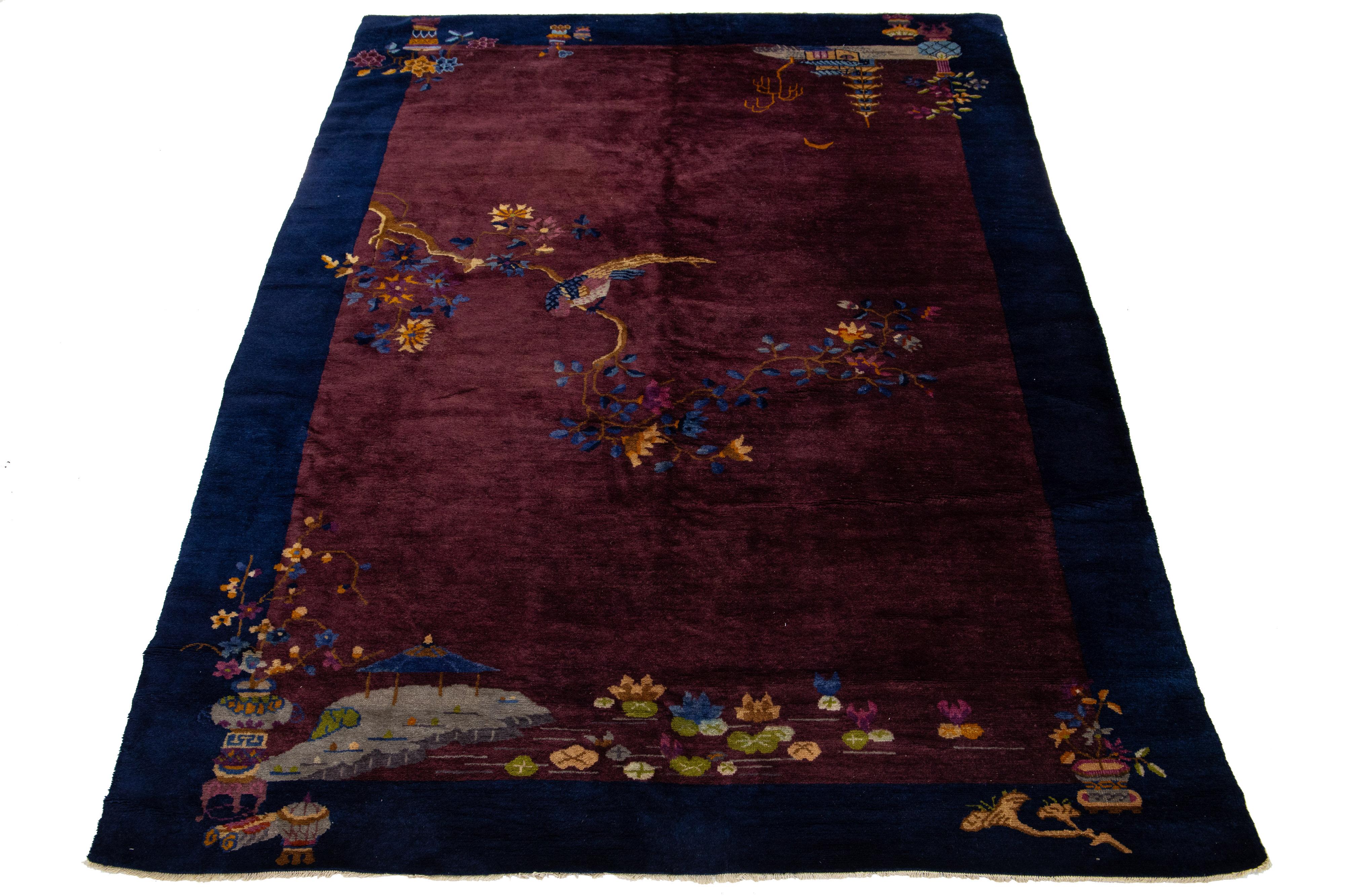 Esta impresionante alfombra antigua de estilo Art Déco chino está expertamente anudada a mano con lana de primera calidad. Presenta un rico fondo burdeos adornado con un vibrante diseño floral multicolor, elegantemente enmarcado por un borde azul
