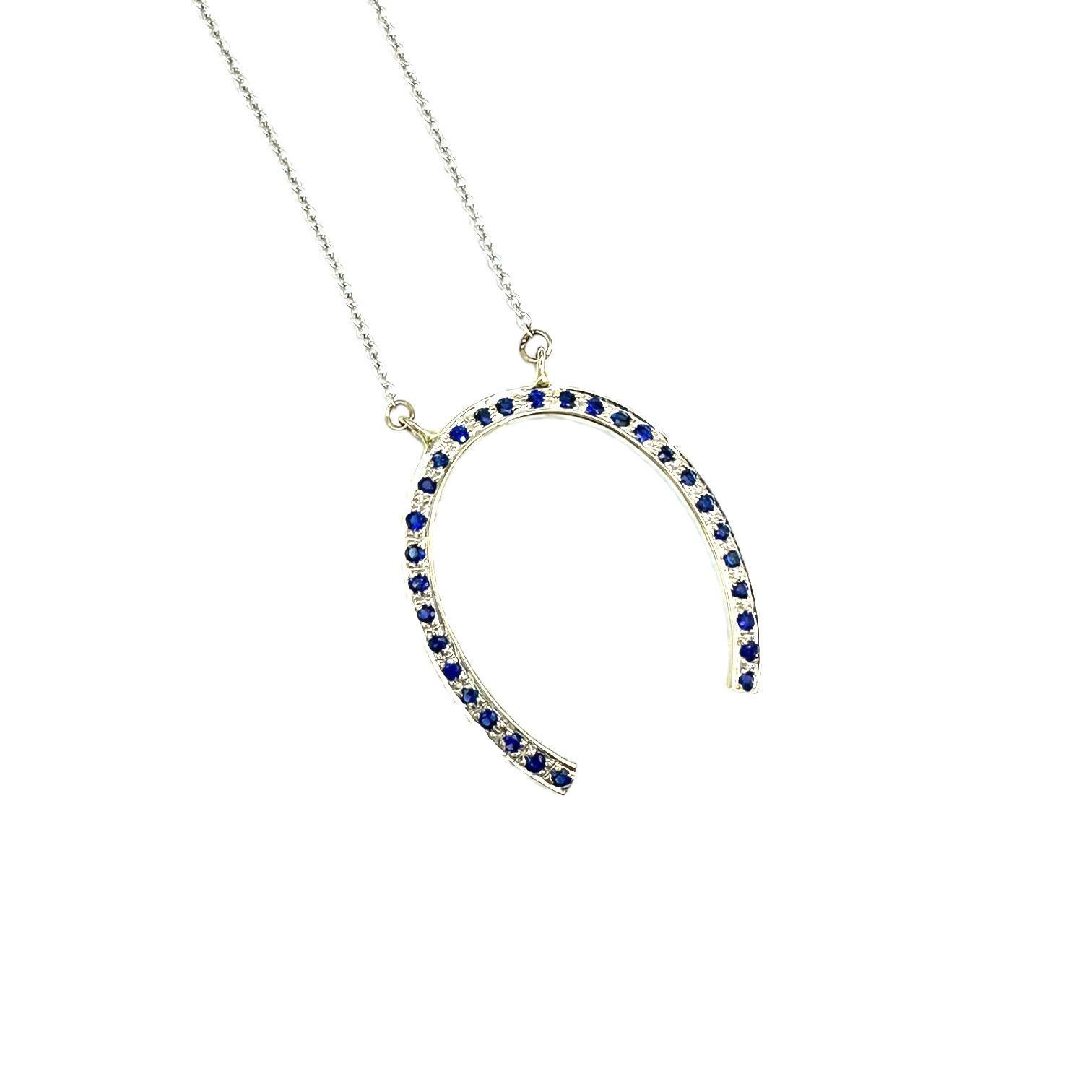 14 Karat white gold horseshoe necklace consists of blue sapphires. The sapphires are pave set in a 1-inch diameter pendant and attached to a 18