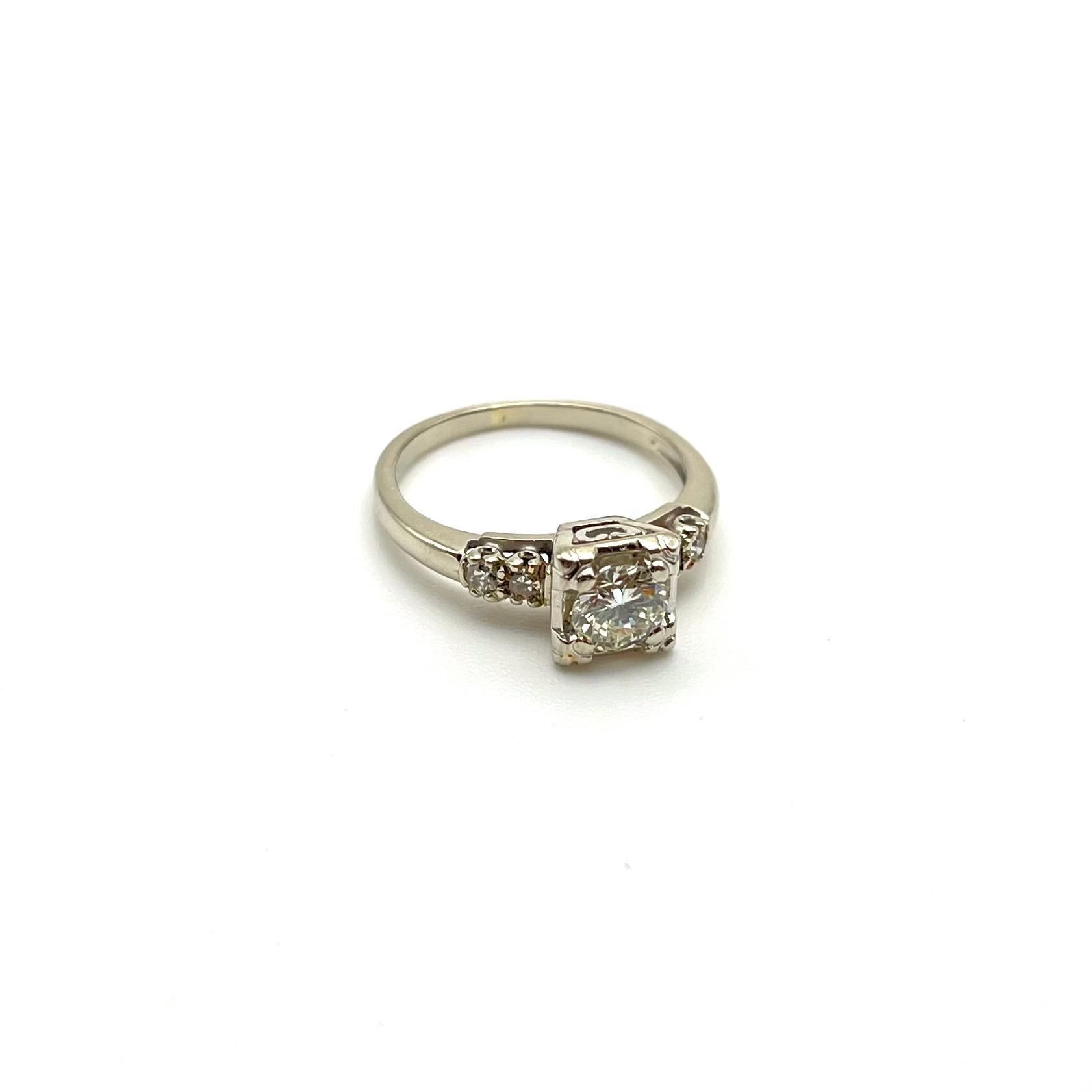 Questo bellissimo anello di fidanzamento in stile vintage è incastonato in oro bianco a 14 carati. Presenta una pietra centrale a taglio rotondo di circa mezzo carato. È affiancato da quattro diamanti rotondi a taglio singolo per un peso totale di