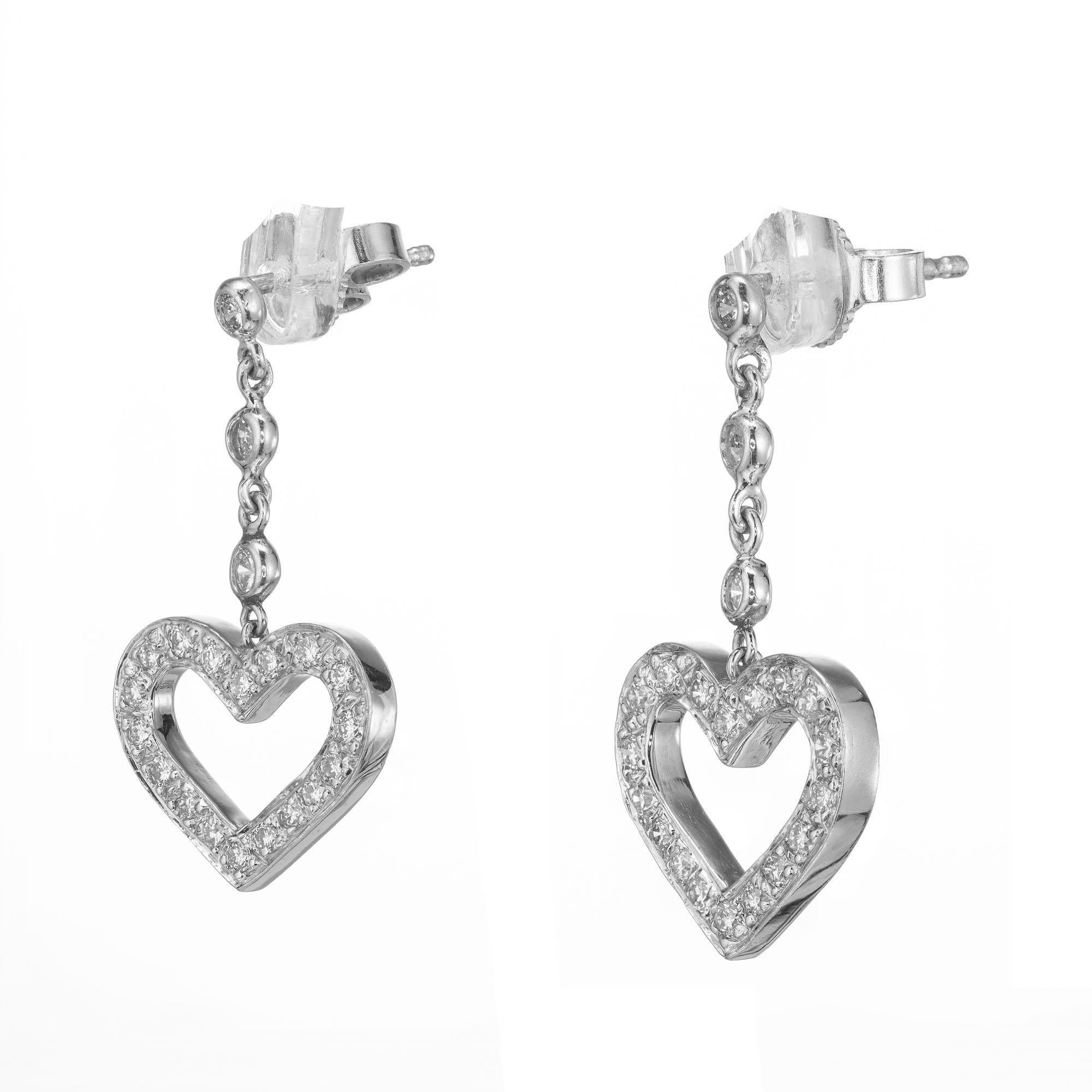 Diamond dangle drop heart earrings. Set in 18k white gold with diamond framed heart dangles. 

42 round diamonds approx total weight. .60 F, VS
Length: .98 inches or 25.04mm
Width: .54 inches or 13.91mm
Stamped: 18k White gold