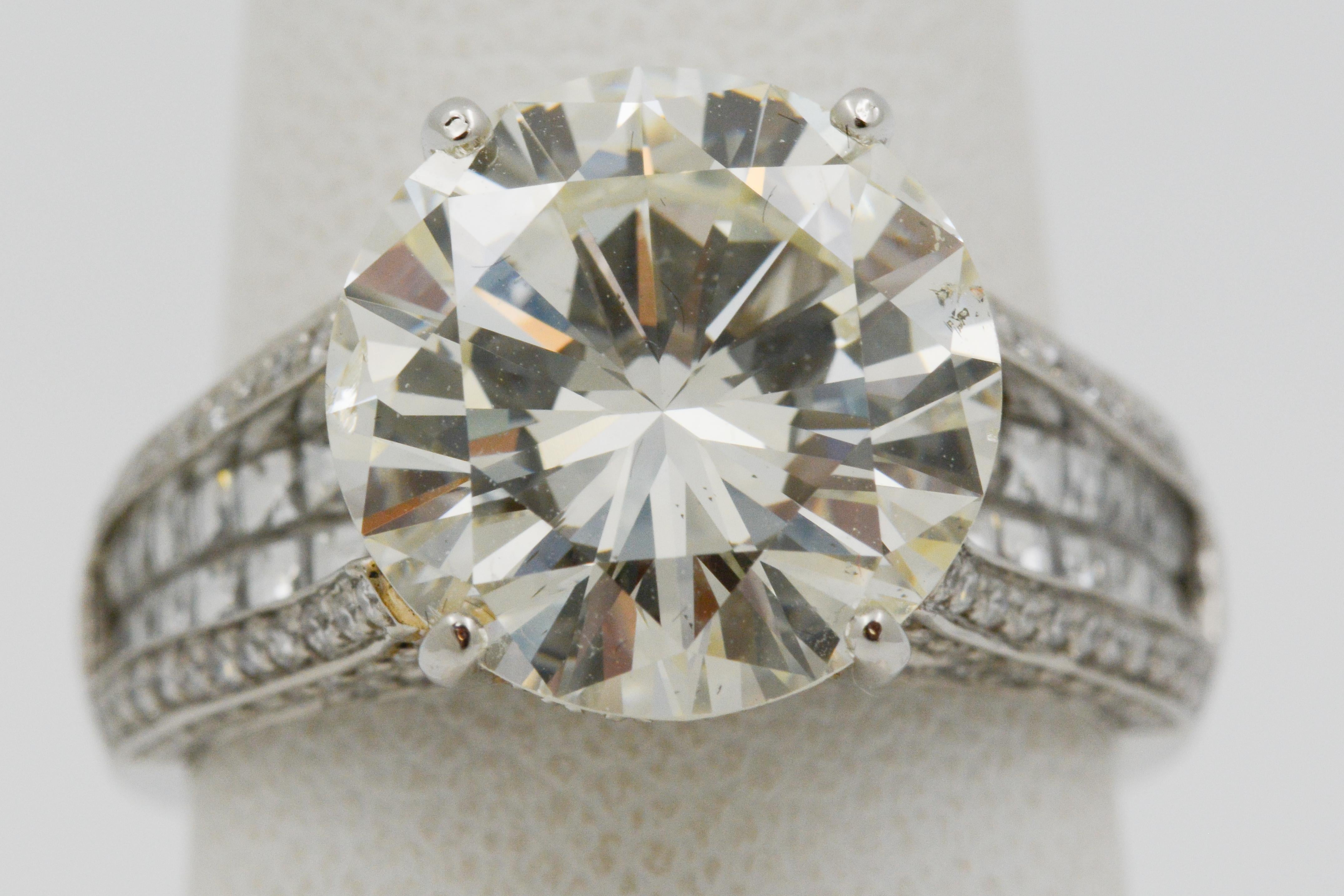 This diamond and platinum engagement ring showcases a 6.01ctw round brilliant cut diamond with M color and SI2 clarity. It also has two rows of blaze cut diamonds in the center row (.73ctw), pave diamonds in the gallery, outer rows and edges half
