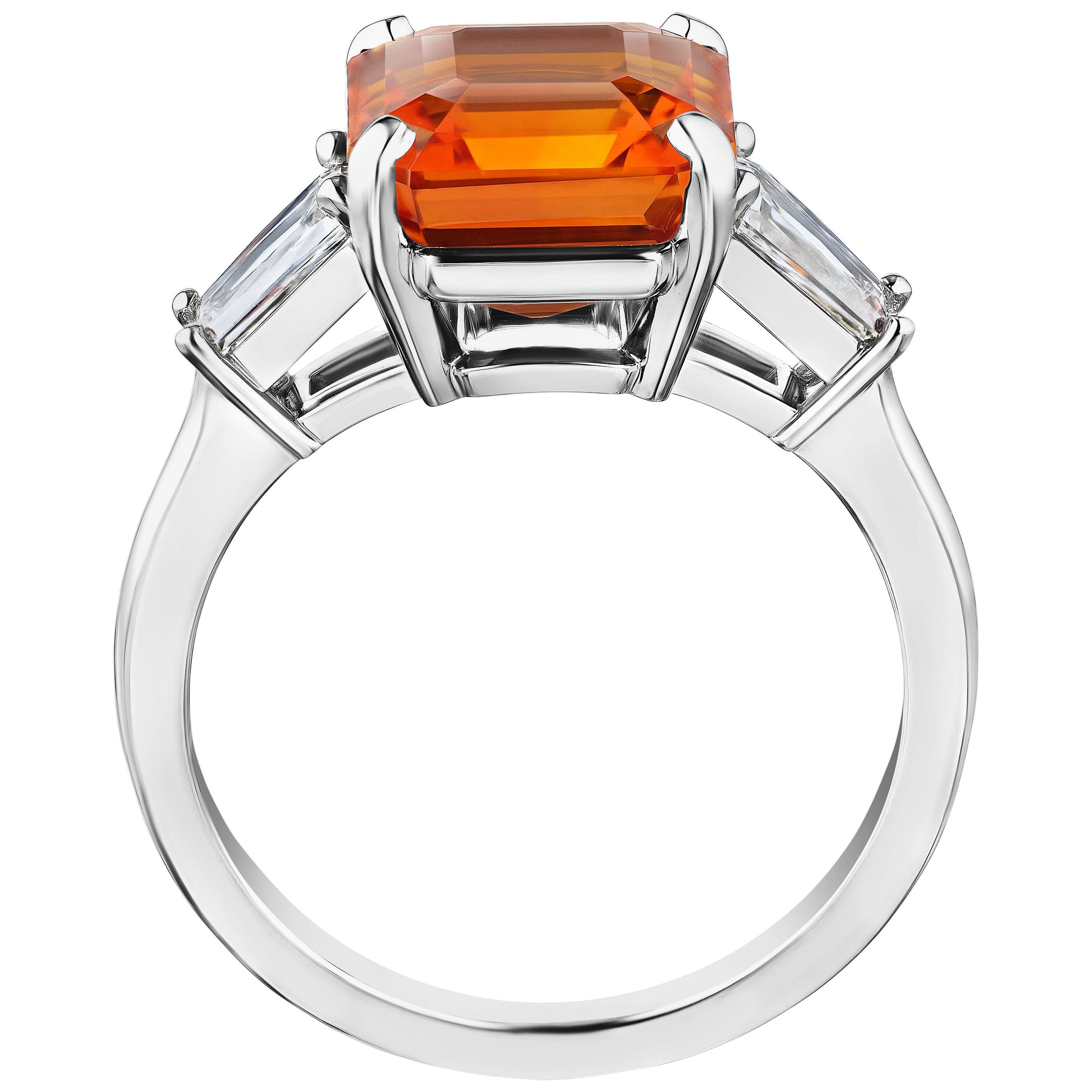 6.01 carat square emerald cut orange sapphire with tapered emerald cut diamonds .89 carats set in a platinum ring. Ring is currently a size 7. Resizing to your finger size is included.