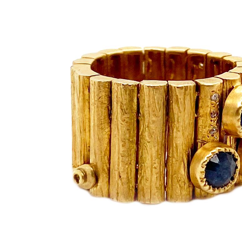 A fun piece to wear to any event, this one of a kind Mosaic Art Deco style flexible ring. Set in 20 karats yellow gold with an approximate 8 Blue Sapphire round stones that weight at 6.03cts and Diamonds at 0.16cts is inspired and brought to you by