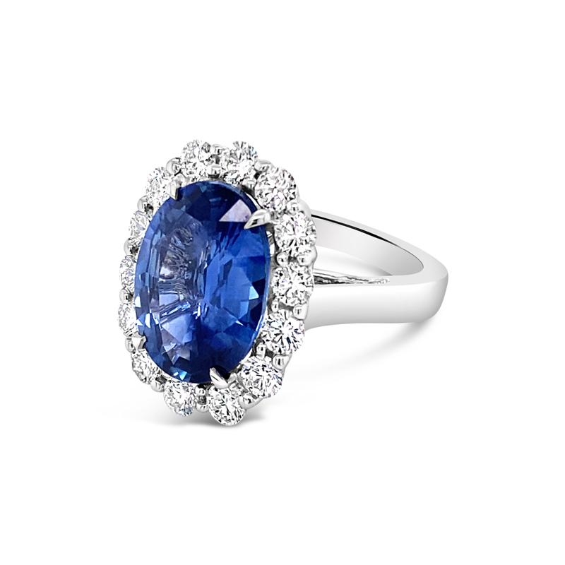 This beautiful cocktail ring features a 6.05 carat oval cut natural blue ceylon sapphire surrounded by 1.40 carat total weight in round diamonds set in 18 karat white gold. It is a size 6 but can be resized upon request. 
Measurements of Sapphire: