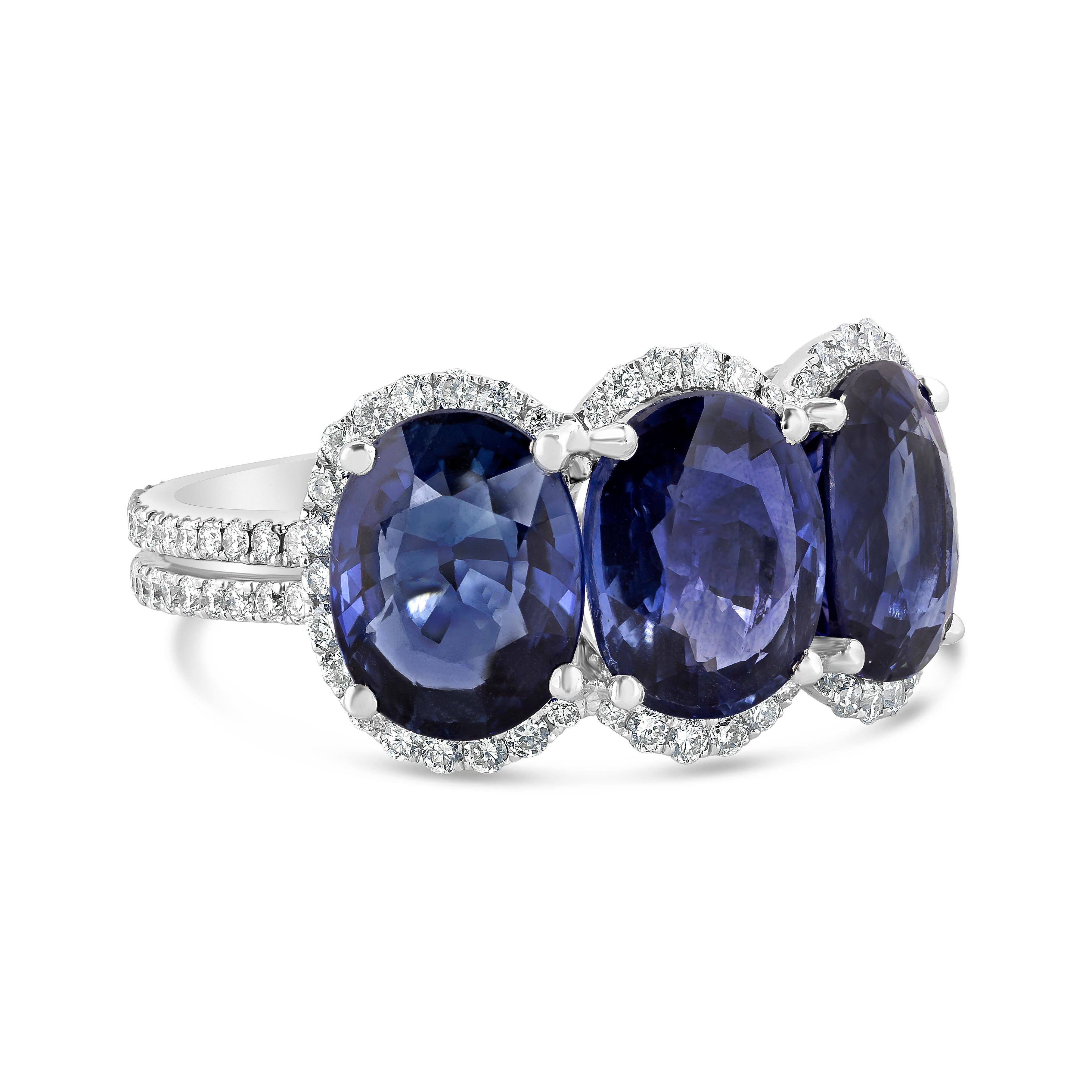 Features a three perfectly matched oval cut blue sapphires weighing 6.07 carats total. Each stone is set in four prong and surrounded by brilliant diamonds halo weighing 0.60 carats total. Set in an accented split shank composition, made in 18K