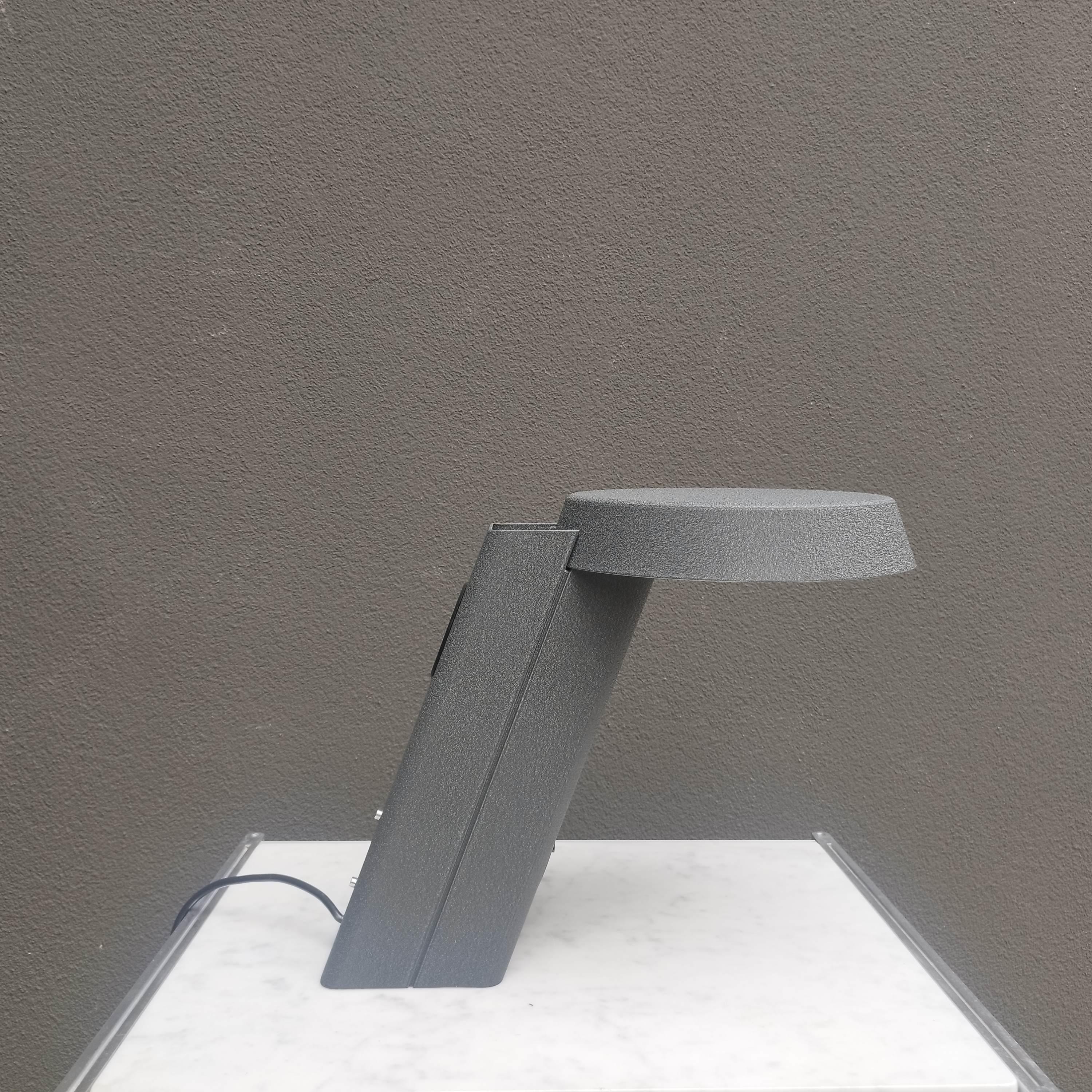 La rara lámpara de sobremesa *Modelo 607*, diseñada por **Gino Sarfatti** para **Arteluce** en 1971, es un sorprendente ejemplo del final de su carrera. La lámpara presenta un escultural cuerpo de aluminio acabado en laca gris texturizada, con un