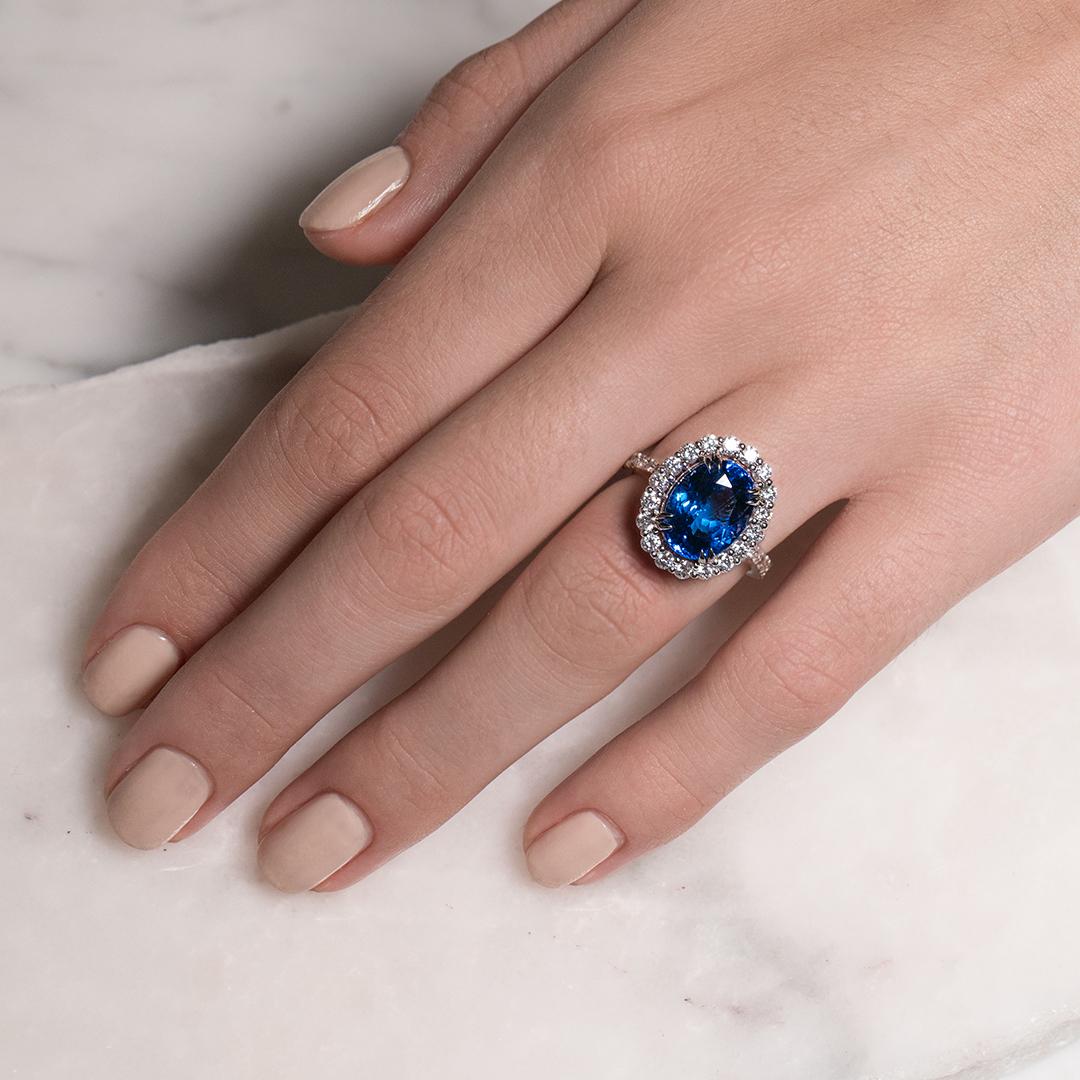 This exquisite Tanzanite Halo Dress Ring features a 6.081ct Oval Tanzanite encased with 1.04ct Round Brilliant Cut Diamonds, set in 18ct White Gold and Black Rhodium to showcase the divine hues of this gemstone. Ring size is M and can be adjusted to