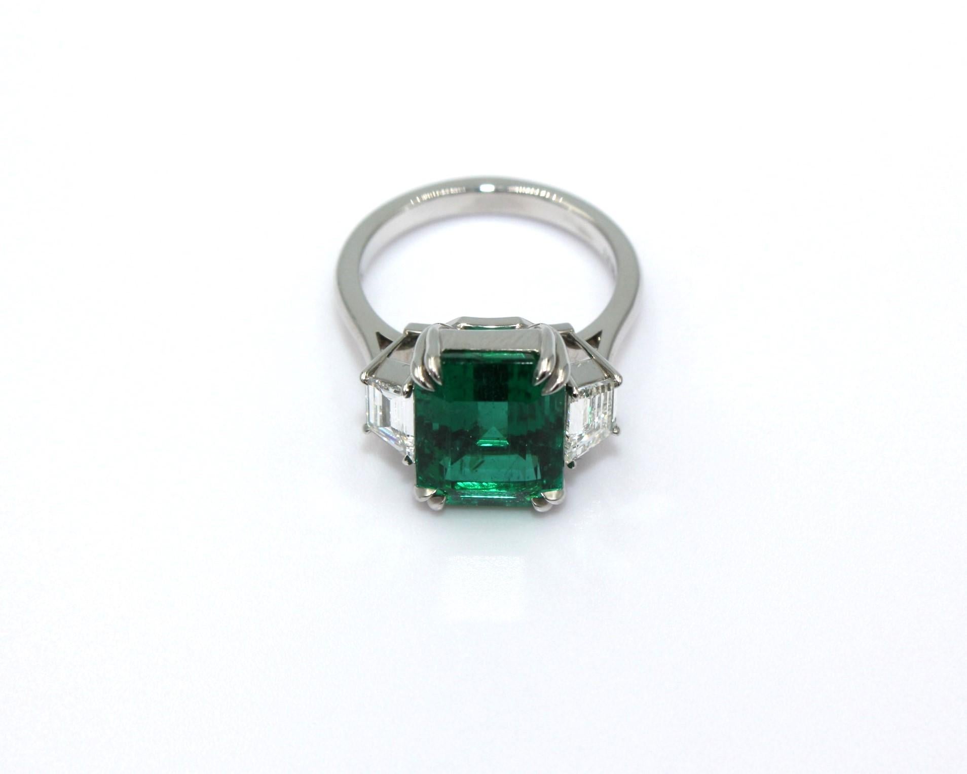 Three-stone ring of 6.09 carat emerald-cut Zambian Emerald with 2 trapezoid shaped diamonds, totaling a diamond weight of 0.70 carat. 

This stunning Emerald Diamond Ring will highlight your uniqueness and elegance. 

Item Details:
- Type: Ring
-