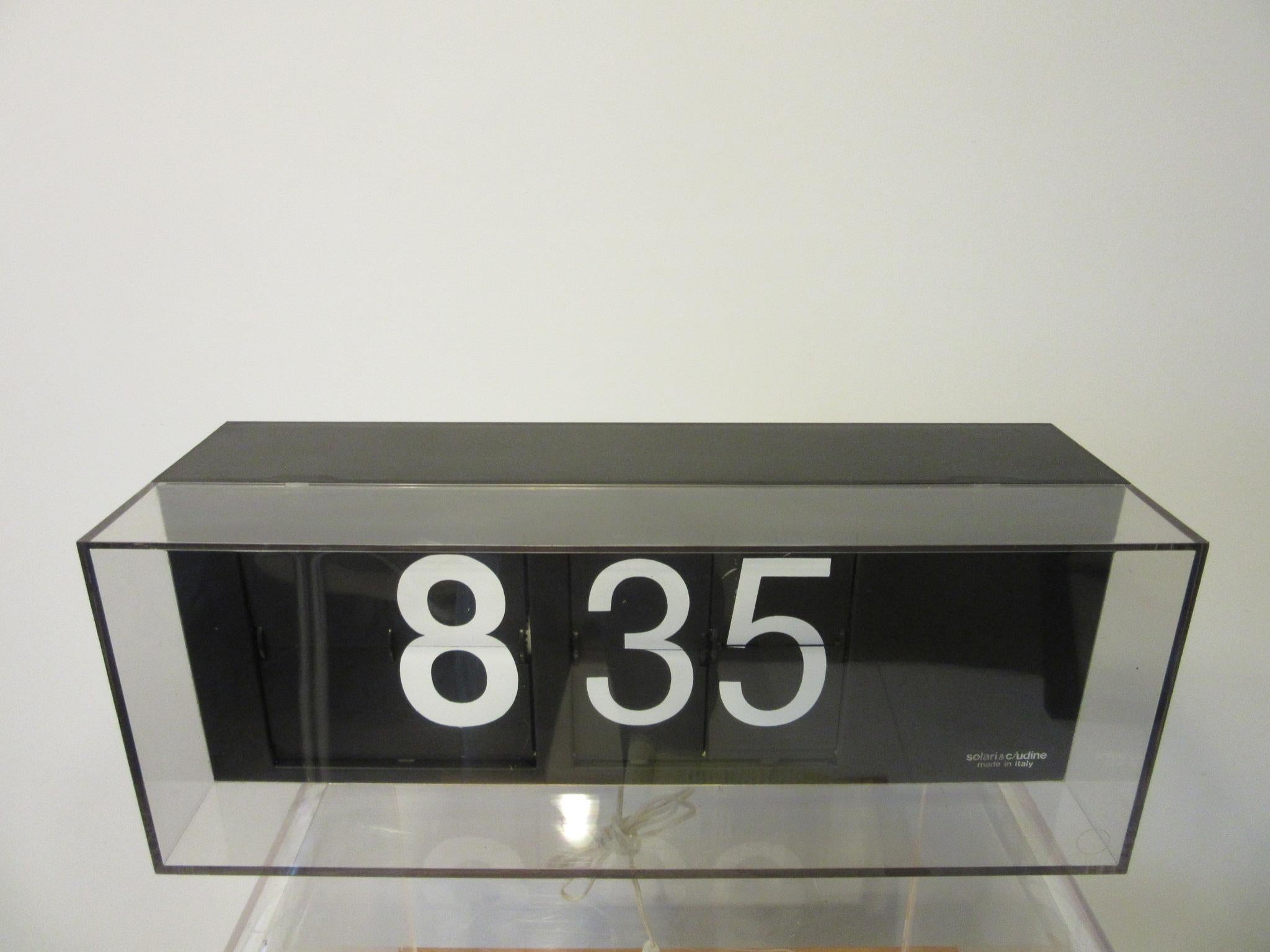 A larger scale Italian flip clock removed from a bank with rectangle case the front in clear plastic and the back in black metal and plastic. To one side are the toggle switches for on / off and to set the time with a lower removable fuse and power