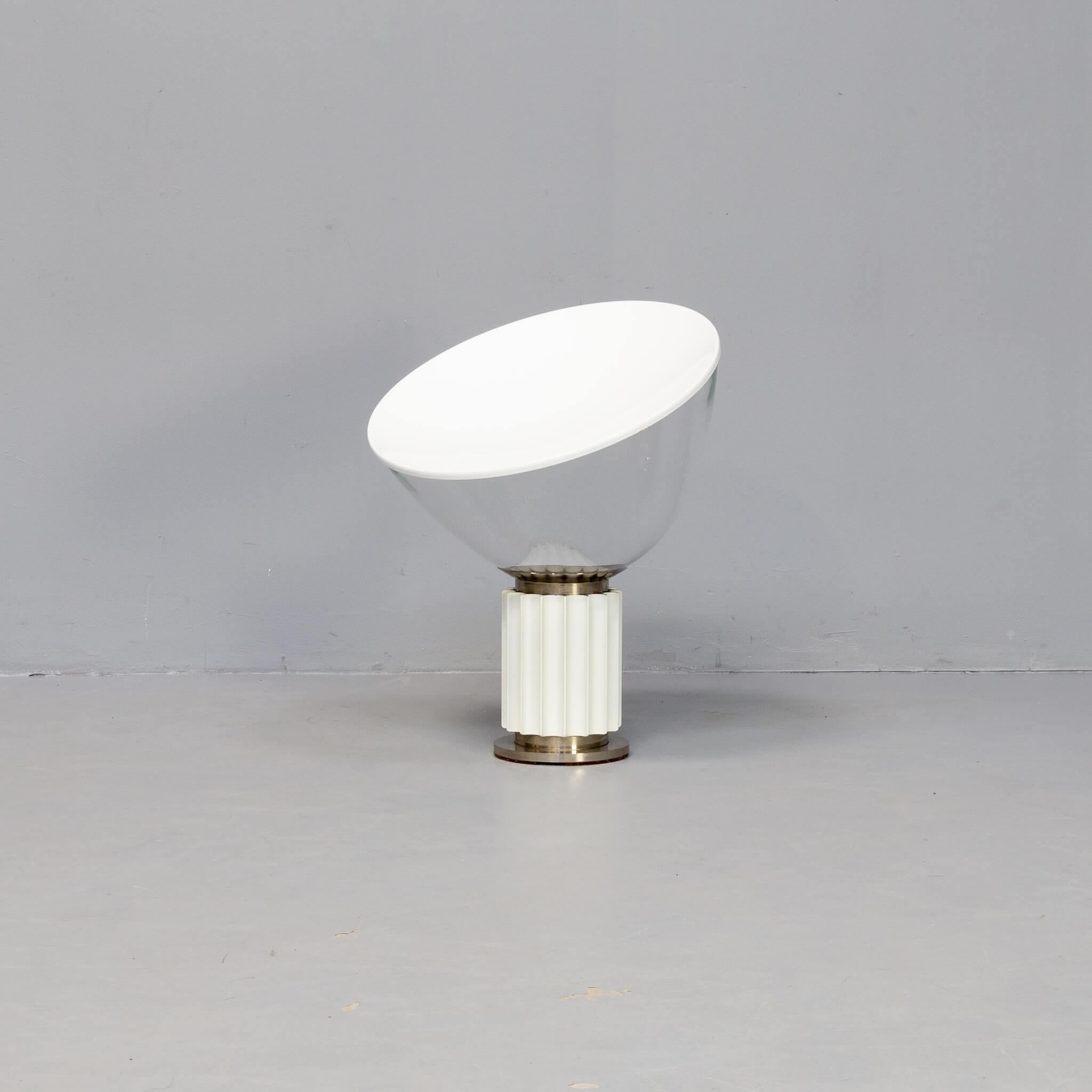 En 1962, les frères Achille et Pier Giacomo Castiglioni ont conçu la lampe de table Taccia pour Flos. Les frères n'ont jamais eu l'intention de concevoir une lampe de table postmoderne. En fait, le principal problème de la lampe était le bol. Les