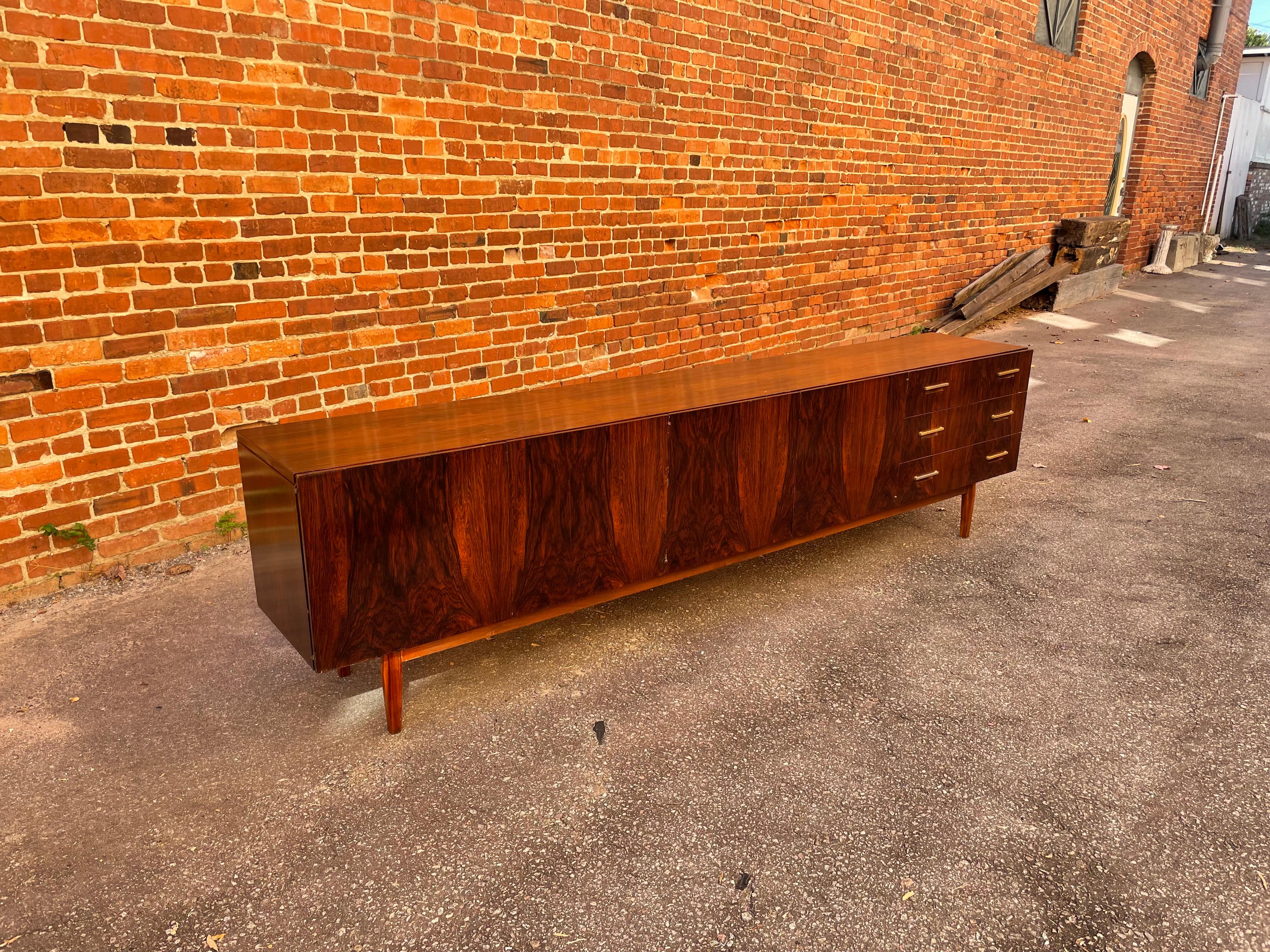 Perhaps a one-time custom order, this monumental Danish style rosewood sideboard, circa 1997 (signed by the maker at the back) features include pivot hinges, four doors, three drawers (including a striped felt-lined jewelry or silverware drawer),