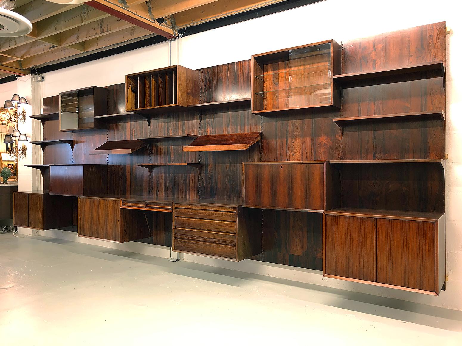 This particular system is commonly referred to as ‘Cado’ to differentiate it from the ‘Royal System', also designed by Poul Cadovius. 
The spectacular rosewood wall system is in really lovely condition showing only minimal signs of its previous