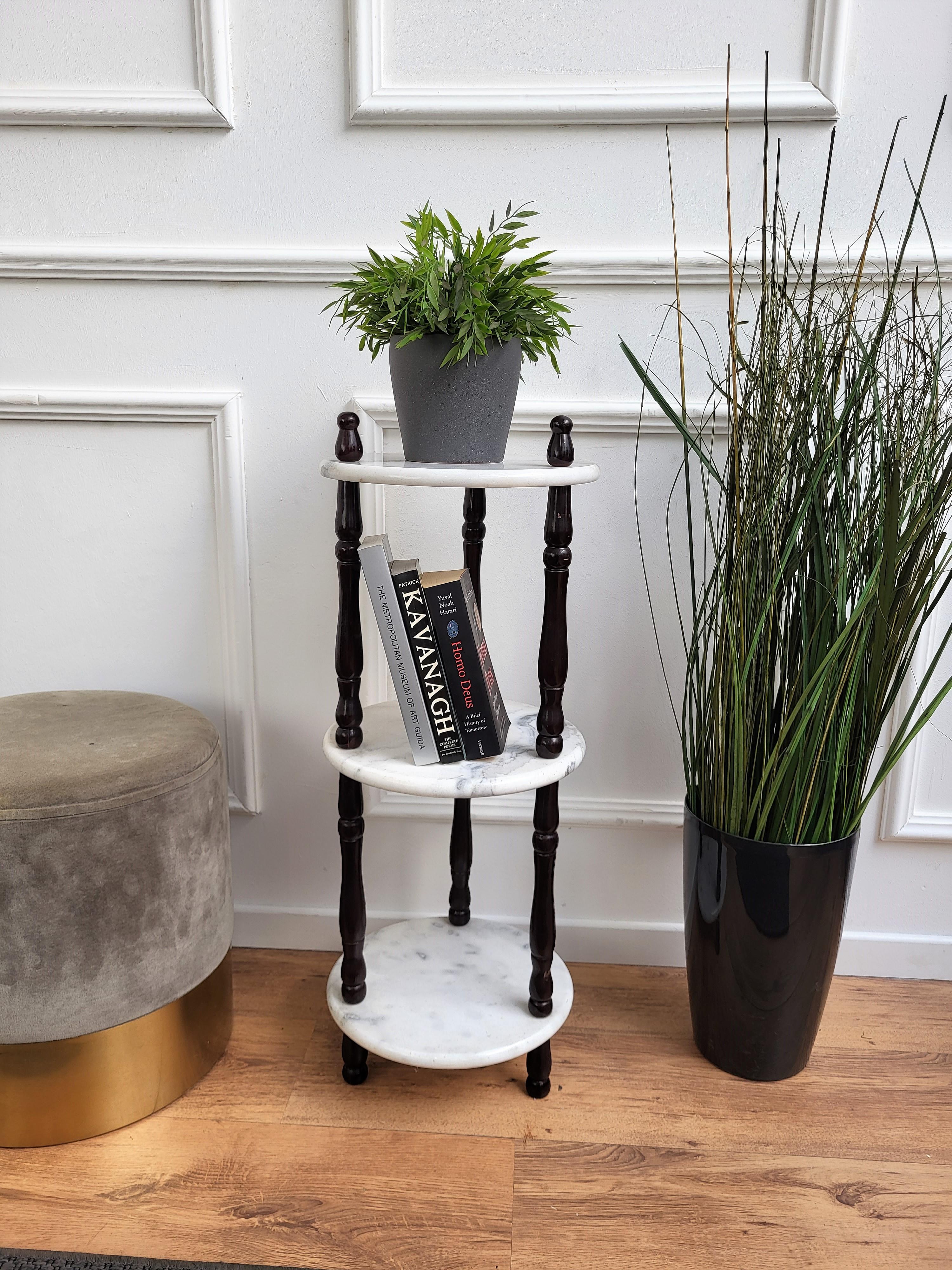 Preciosa y muy elegante mesita auxiliar o etagere italiana de mármol de mediados de siglo. Esta pieza se estructura en torno a tres columnas o patas de madera negra tallada con tres estantes o gradas redondas de mármol blanco de carrara. Las formas