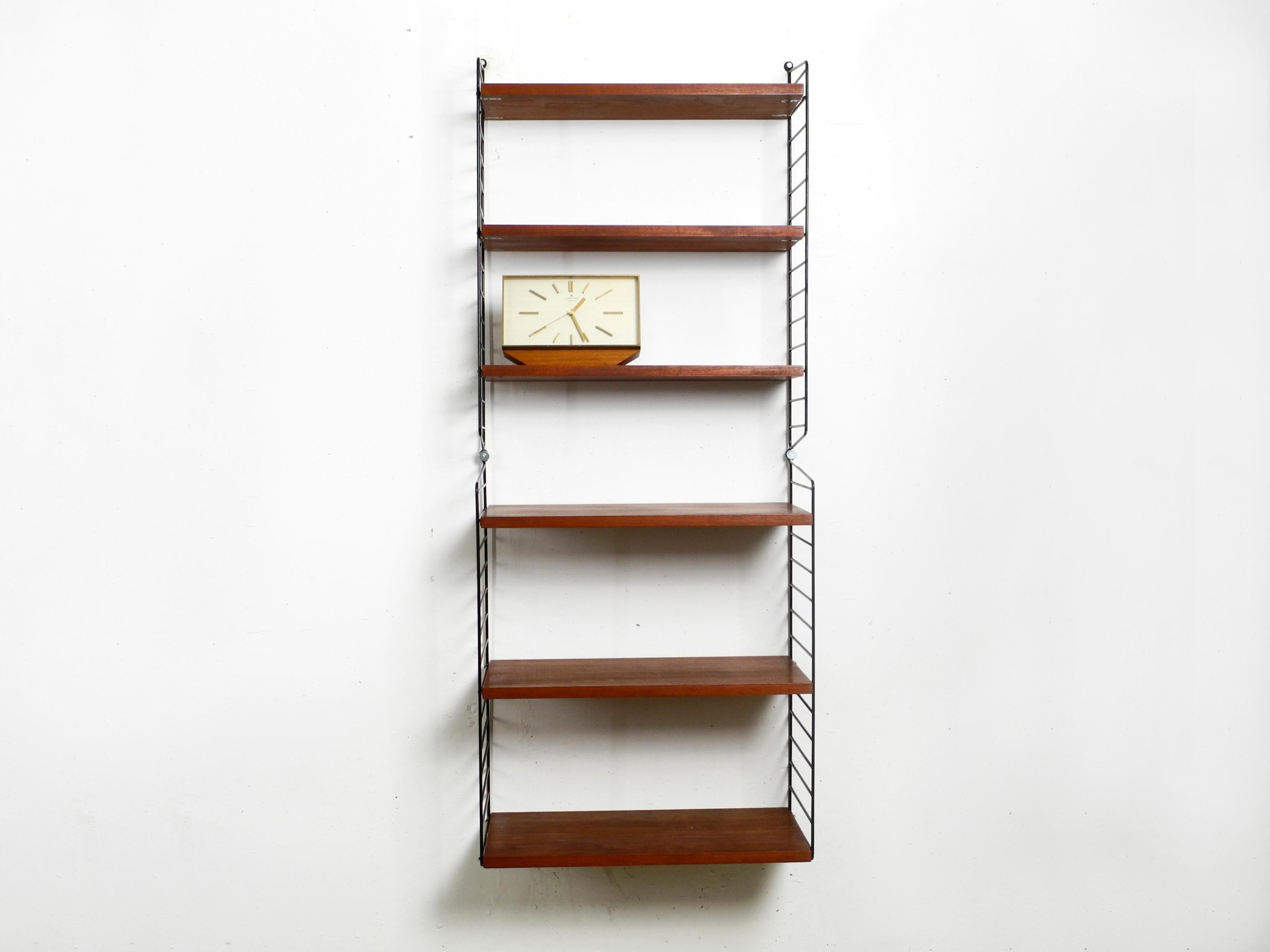 Original narrow 1960s Nisse Strinning shelf. This string shelf has dark teak shelves with 20cm and 30cm depth. Made in Sweden. 
Two ladders and 3 boards have a depth of 20 cm, two ladders and three boards have a depth of 30 cm.
All shelves are 58 cm