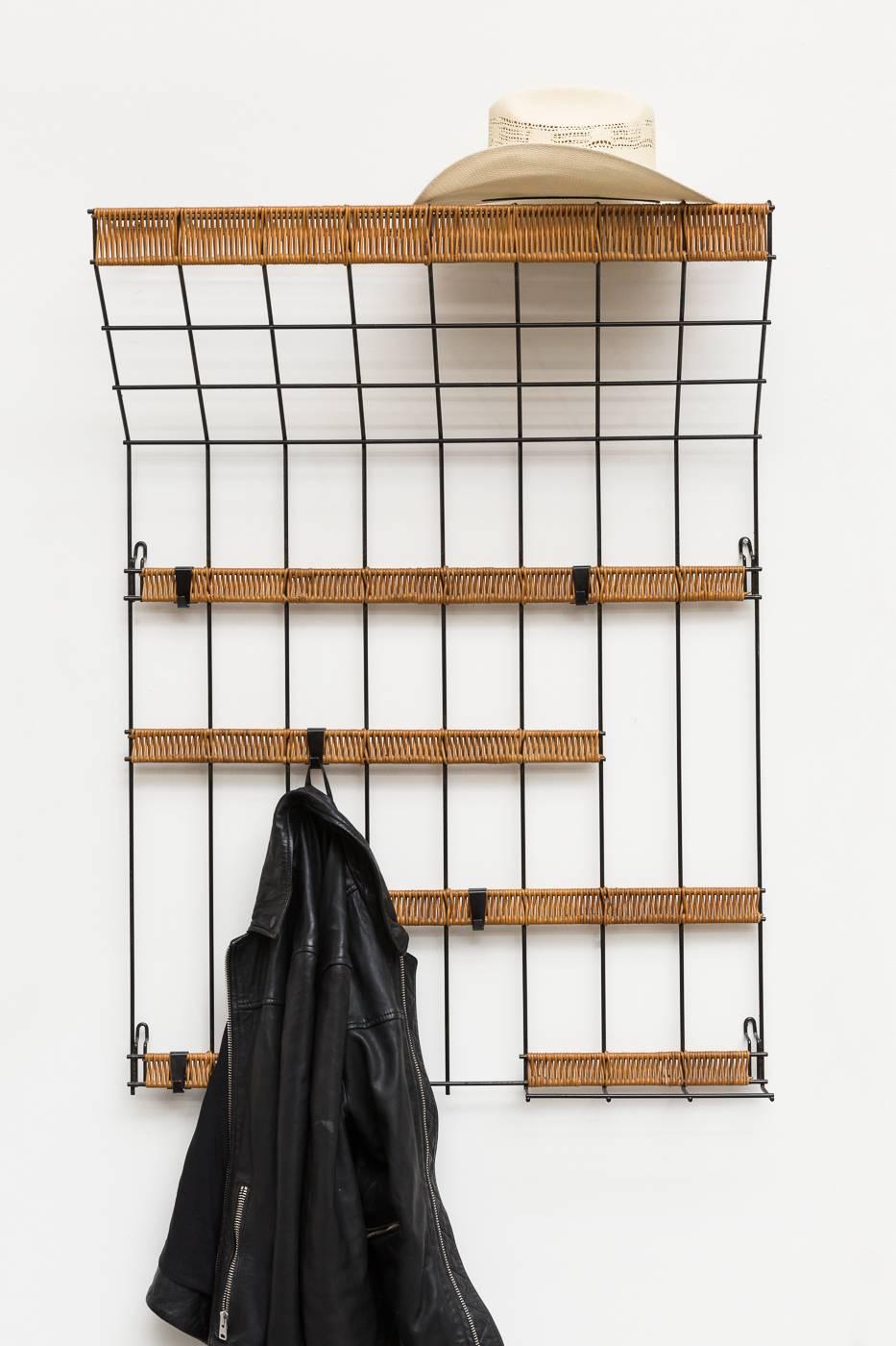 Black enameled metal wire grid wall mount coat rack with woven rattan detail and removable hooks. Very good original condition.