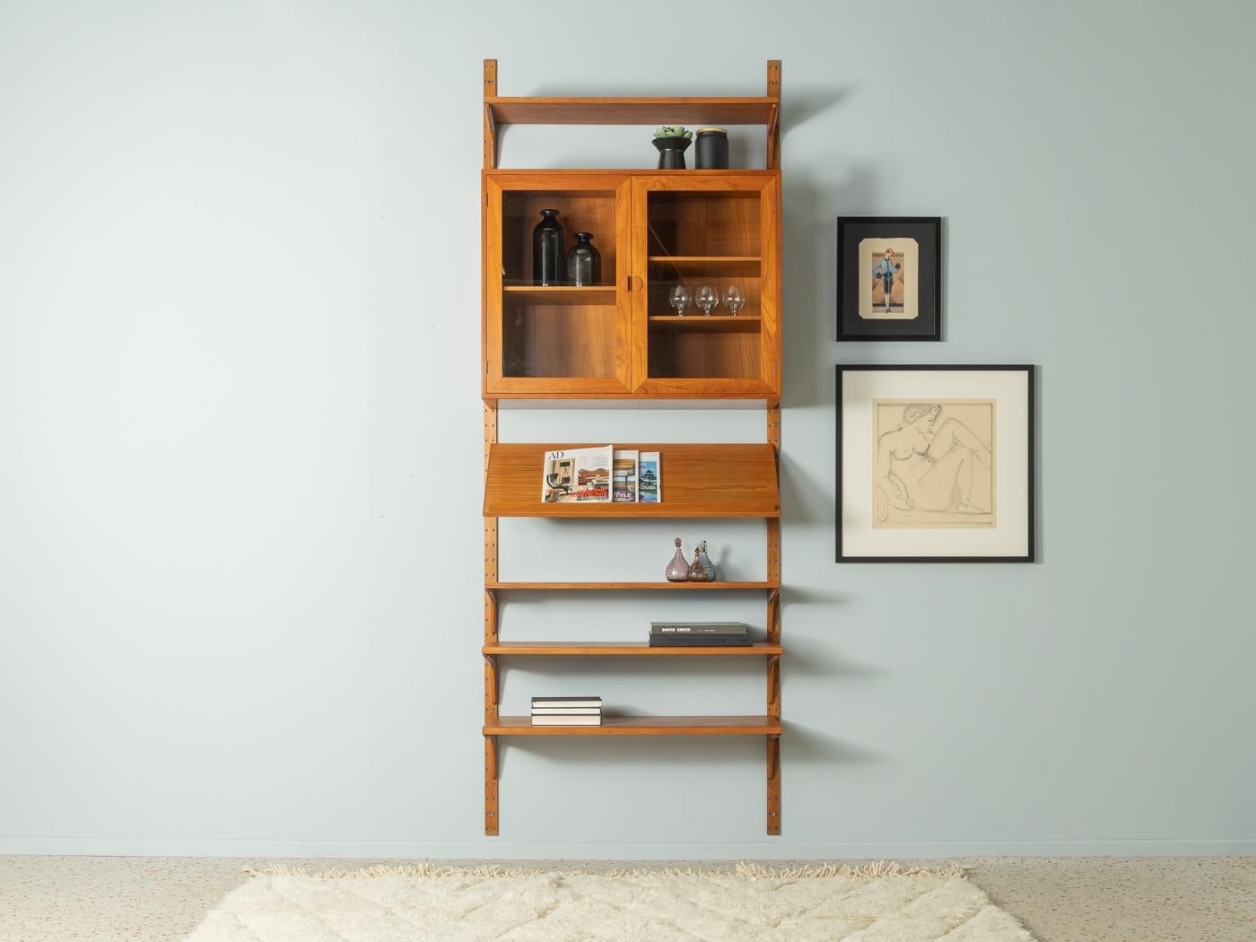 Classic shelving system from the 1960s by HG Furniture. The high-quality containers and shelves are veneered in teak. The system consists of one container with glass doors, four shelves, a magazine rack and two ladders.

Quality features:
