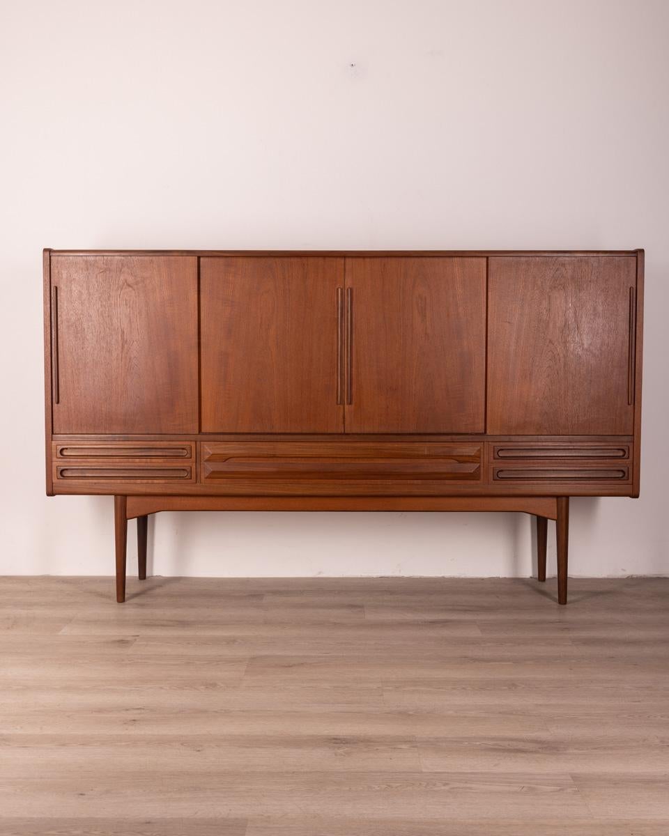 Highboard sideboard in Teak wood, has four sliding doors and five drawers at the bottom.
Design by Jhoannes Andersen for Uldum Møbelfabrik, 1960s.

Conditions: In good condition, it shows signs of wear given by time.

Dimensions: Height 131 cm;