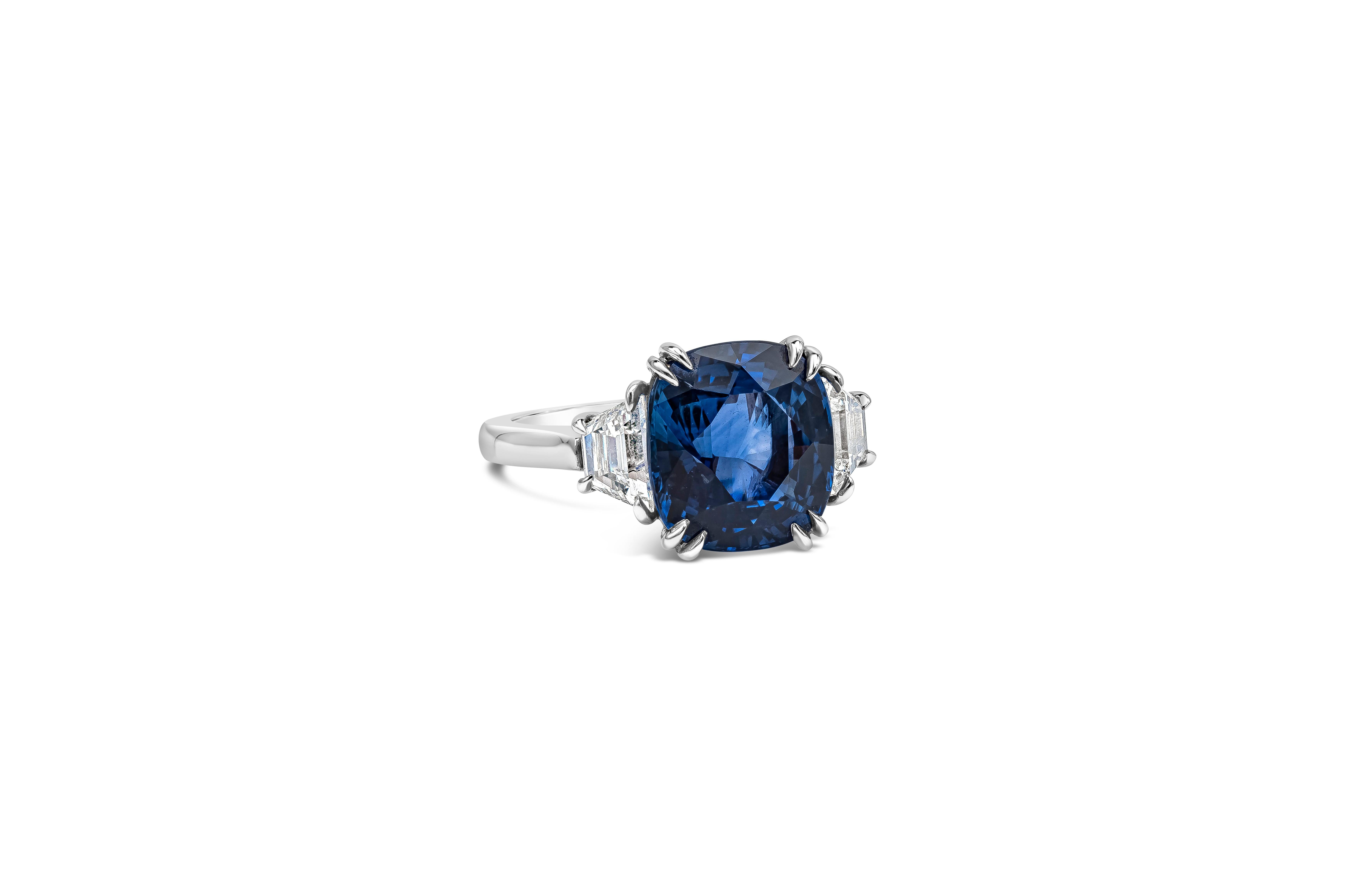 A stunning three-stone engagement ring, showcasing a 6.10 carats cushion cut blue sapphire, set on a four double claw prong setting. Flanked by step cut trapezoid diamonds weighing 0.96 carat total with G color and SI clarity. Finely made with a