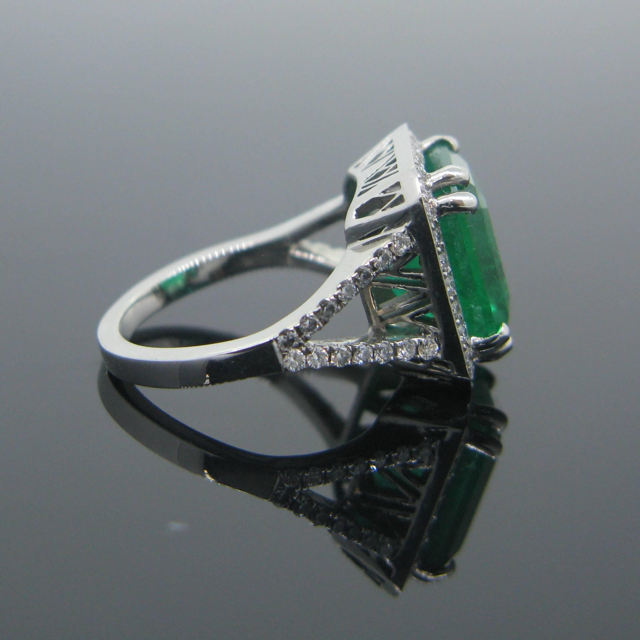 This stunning new ring is made in platinum and features a magnificent 6.14ct Colombian emerald with a vibrant green color. The stone is surrounded with 30 small diamonds and 28 diamonds on each side of the ring. Emerald is also known as the stone of