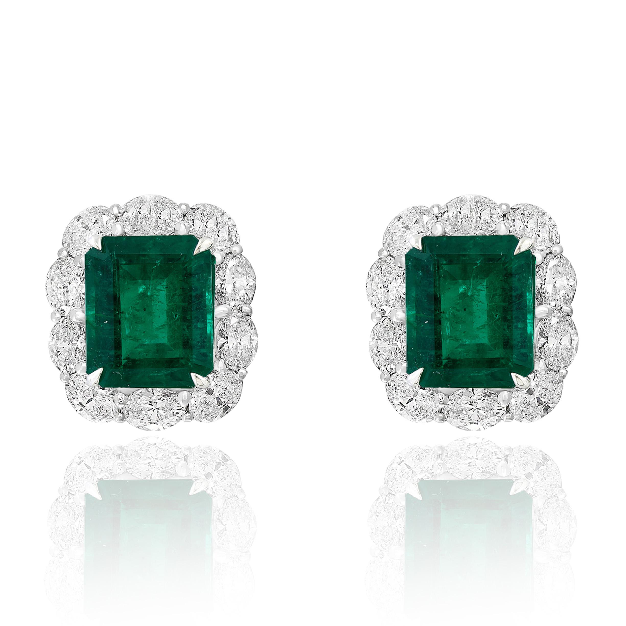 Showcasing two color-rich Emerald cut Lush Green Emeralds weighing 6.15 carats total, surrounded by a single row of oval-cut brilliant diamonds. 20 Accent diamonds weigh 2.91 carats in total. Set in 18 karats white gold. Omega Clip with the