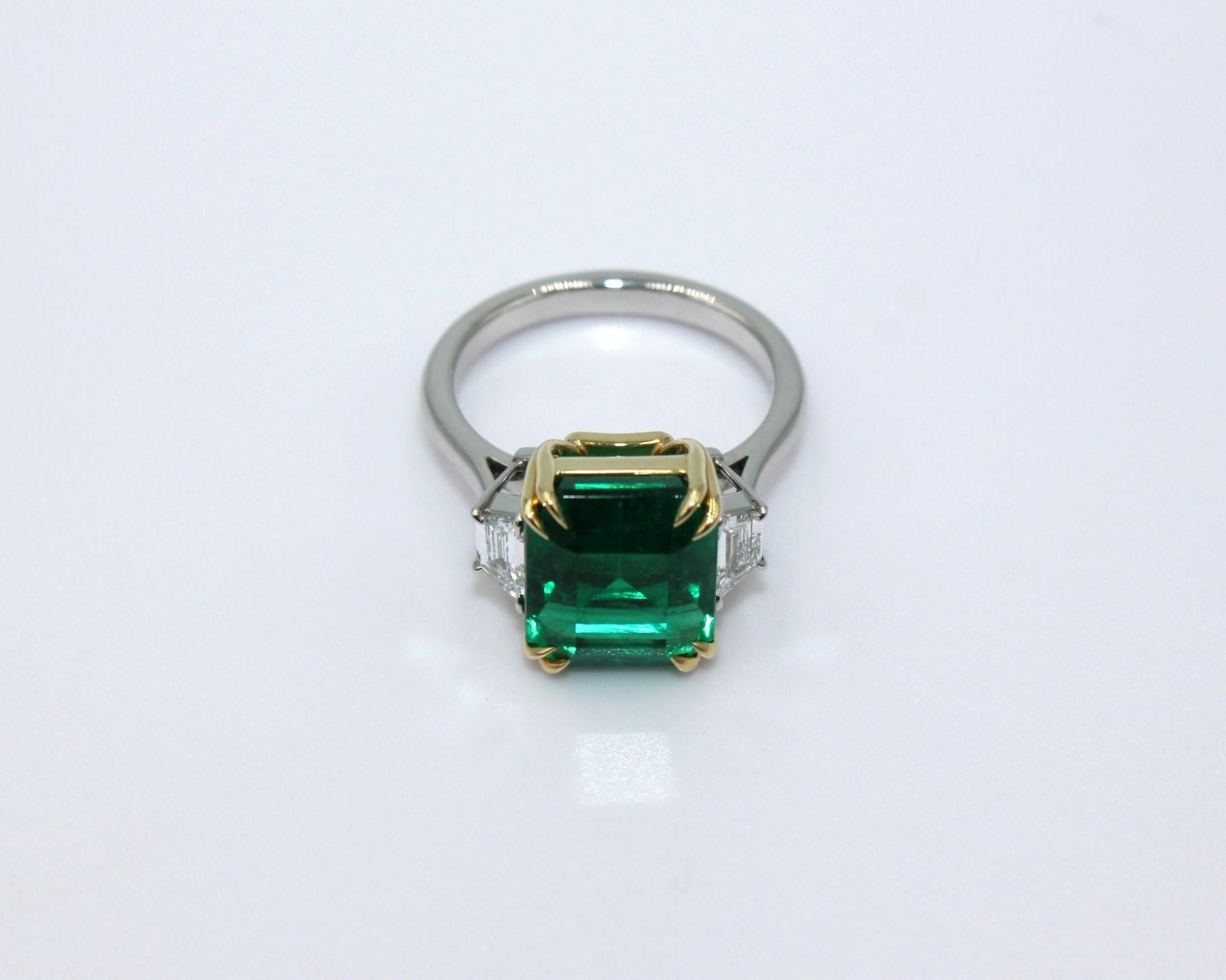 6.16 carat emerald-cut Zambian Emerald with 2 trapezoid shaped diamonds, totaling a diamond weight of 0.48 carat. 

This stunning Emerald Diamond Ring will highlight your elegance and uniqueness. 

Item Details:
- Type: Ring
- Metal: 18K Gold &