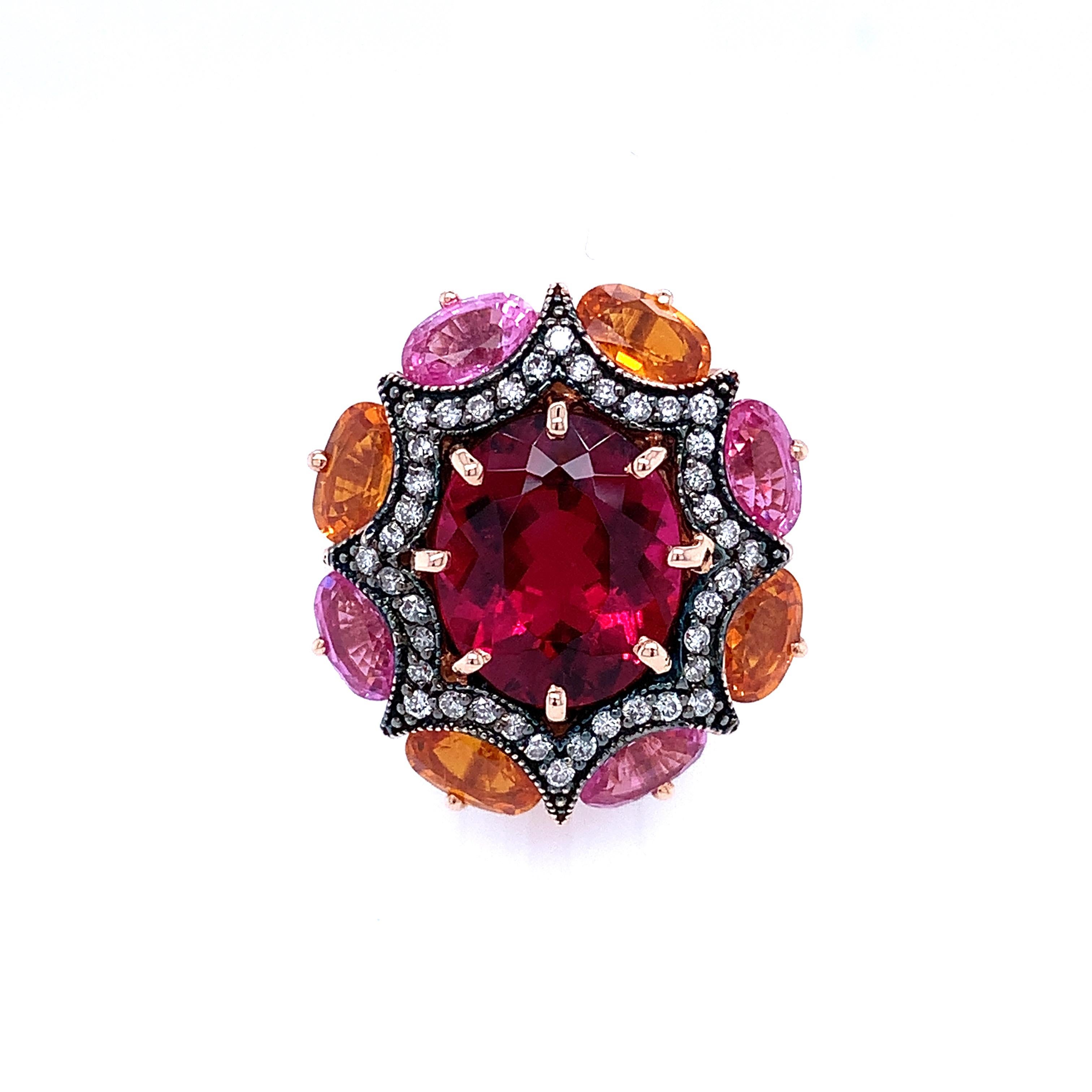 This bold cocktail ring features a luscious 6.23 carat, rubellite tourmaline oval surrounded by a starburst frame of diamonds set in rose gold with a dramatic black rhodium finish. The outer frame of this festive 18k rose gold ring is set with