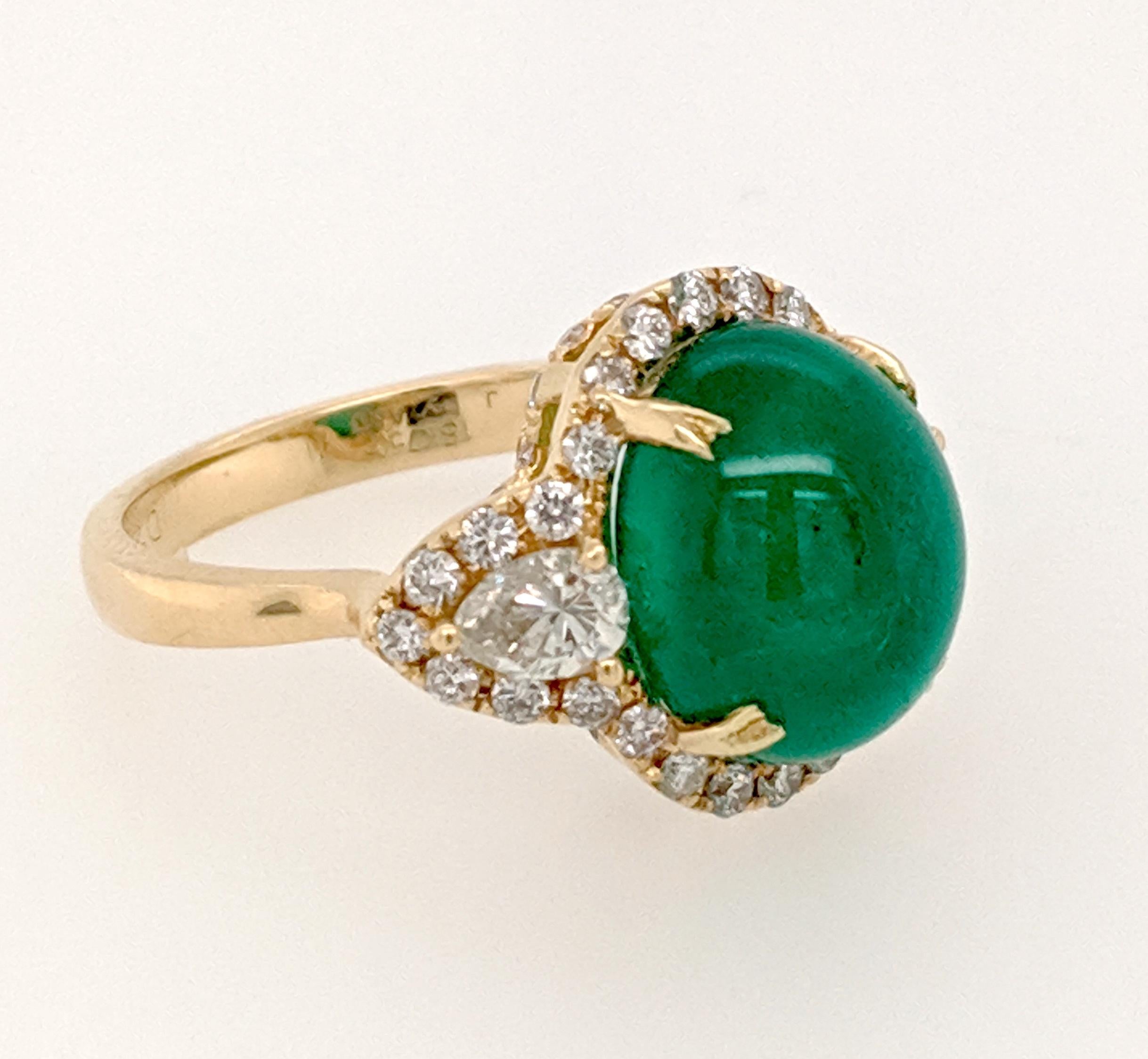 The Cocktail Ring is crafted in 18k yellow gold and features (1) Cabochon emerald weighing approximately 6.25ct and flanked by (2) pear shaped diamonds weighing approximately .53cttw with a color of H/I and a clarity of SI1. The mounting also has