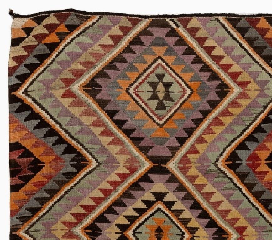 Vintage Turkish hand-woven flat-weave (Kilim) runner rug was made with 100% wool. It has flat wool pile and features a dynamic and colorful design of nested lozenges with serrated edges in orange, terracotta, light blue, sage green, faded yellow,