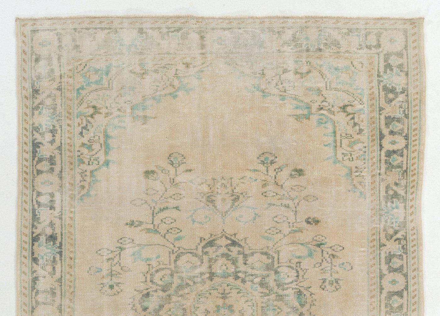 A mid-century Turkish area rug hand-knotted in the 1960s with low wool pile on cotton foundation. It features a medallion with floral tendrils at its center in turquoise green and forest green against a plain beige background and a main border in