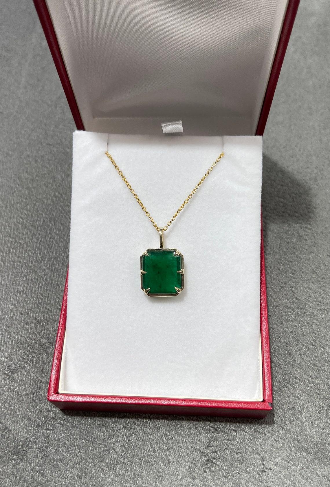 Displayed is a natural emerald Georgian styled solitaire pendant in 14K yellow gold. This gorgeous solitaire pendant carries an earth-mined emerald in a prong setting. Fully faceted, this gemstone showcases excellent shine. The emerald has good