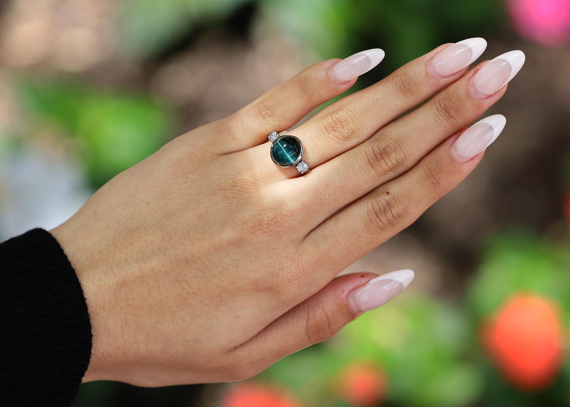 ¿Llevarías esta intrigante turmalina indicolita de ojo de gato como anillo de compromiso de 3 piedras o anillo de cóctel? El vibrante azul verdoso de esta gema parlanchina con un hipnotizante 