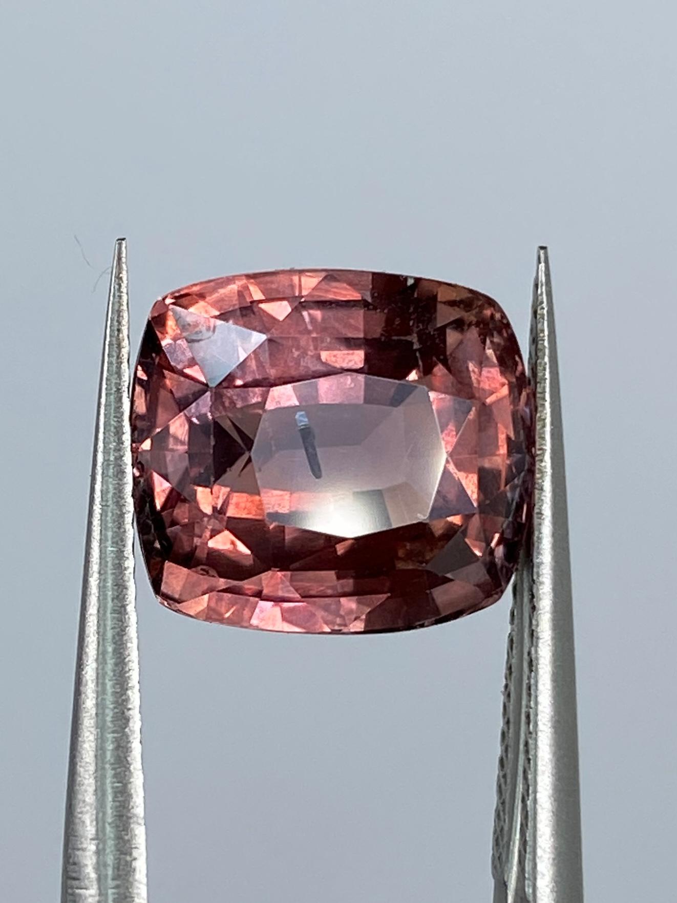 The Sapphire Merchant is proud to present this sensational Padparadscha Sapphire. At a remarkable 6.33 carats, this cushion-shaped beauty boasts a Modified Brilliant Cut, ensuring every facet dances with light and exudes unparalleled brilliance.